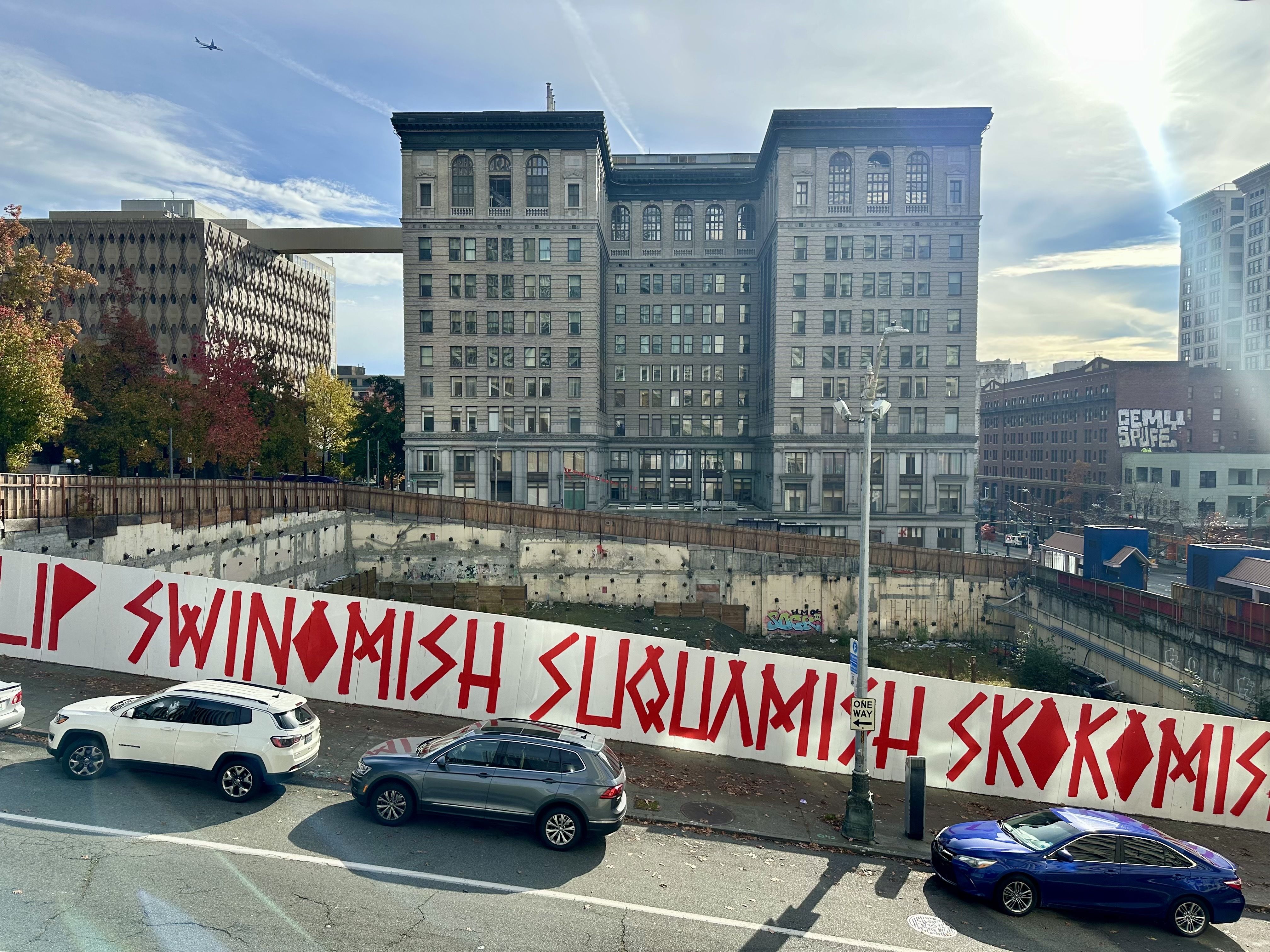 A look at the empty lot with a view down into the hole, looking over Cherry Street where cars are parked on the street and the King County Courthouse is directly behind the vacant lot.