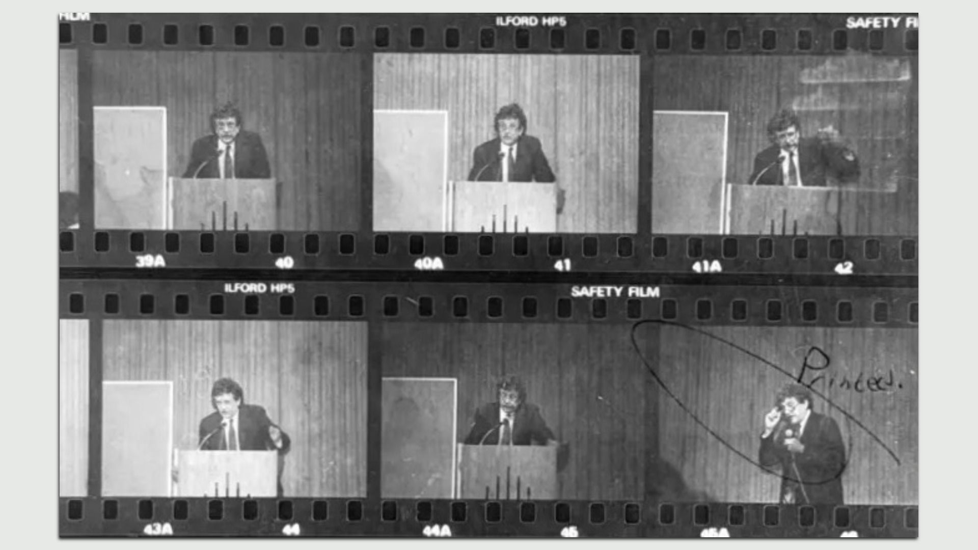 Black and white film strip with six frames showing a man in a suit speaking at a podium against a wood-paneled background. One frame is circled with annotation.