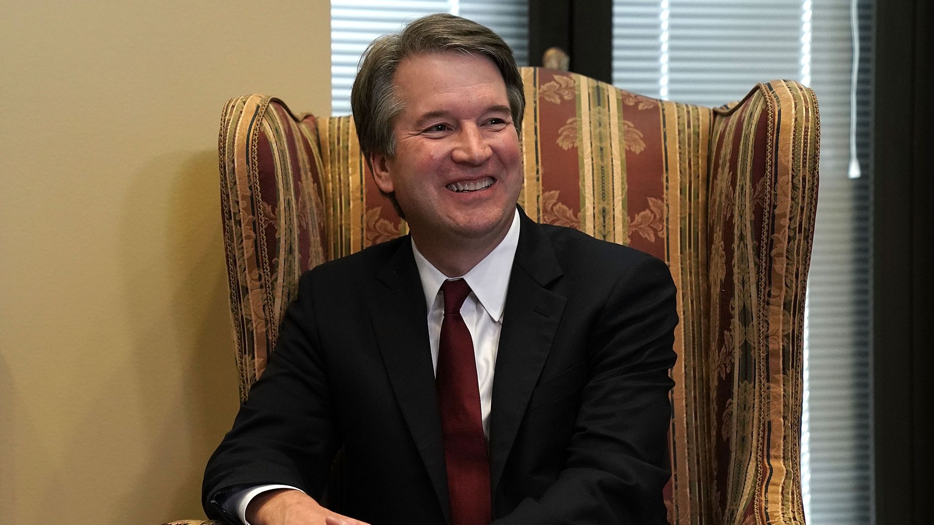 Brett Kavanaugh smiles wide while seated in an armchair