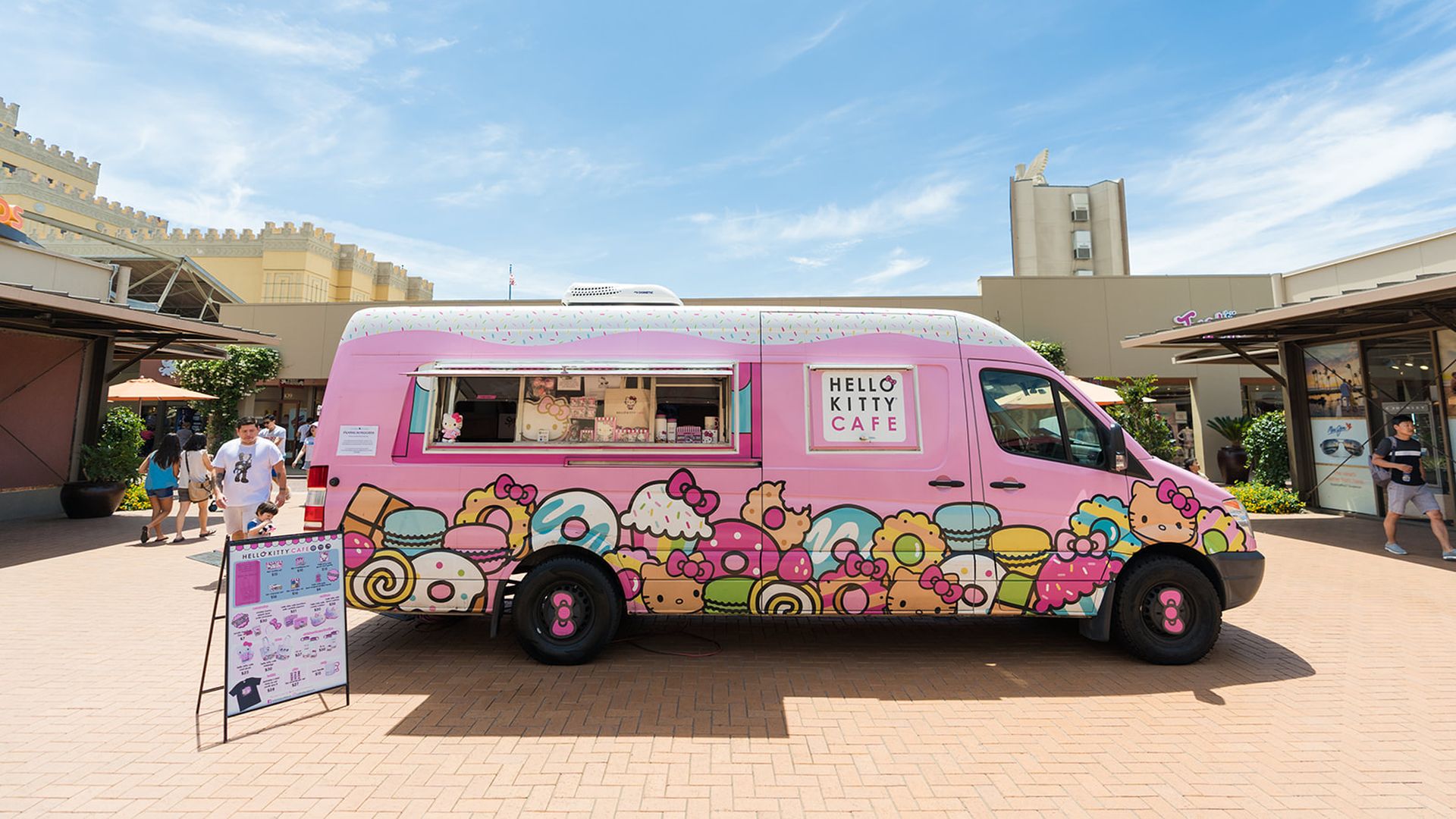 A pink Hello Kitty-themed van parked outside a shopping center. 