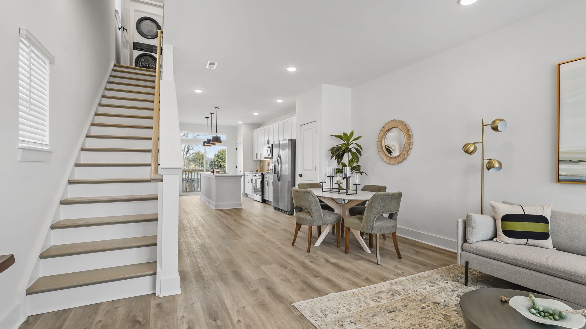 Modern open-concept interior featuring a kitchen, dining area, living room and staircase with neutral tones and contemporary decor.