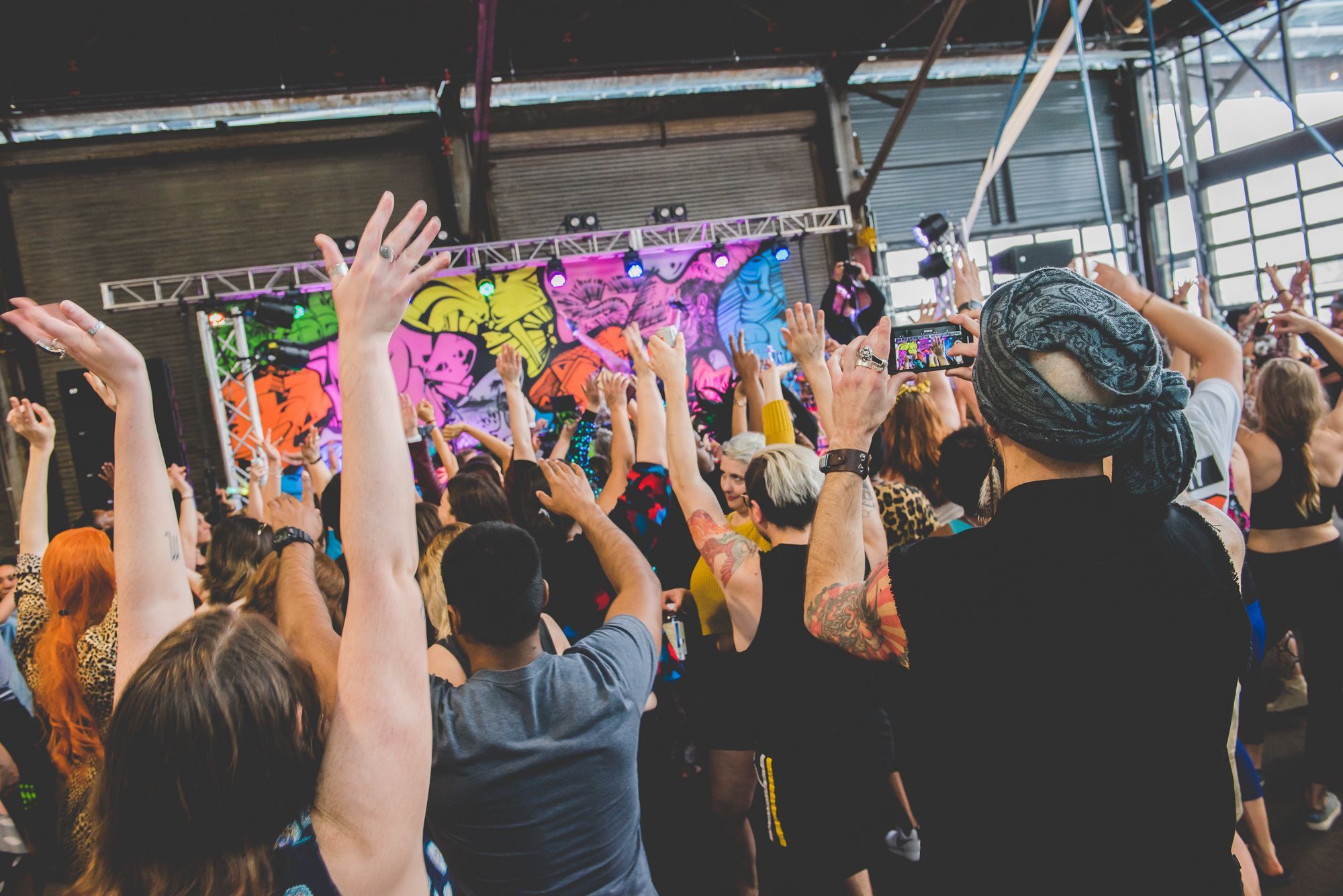 Festival-goers wave their hands in the air in front of a stage.
