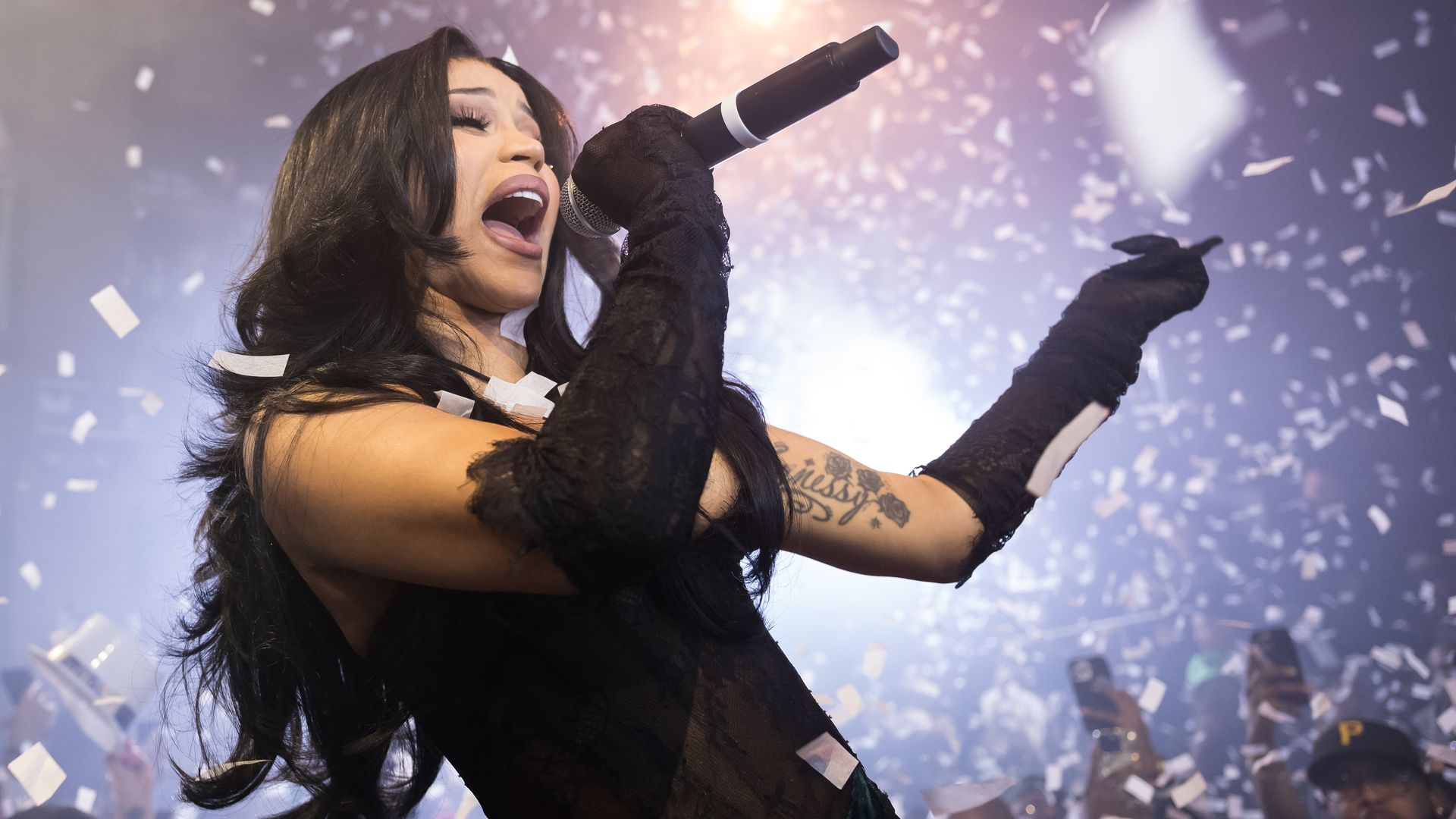 Cardi B sings into a microphone as confetti falls around her.