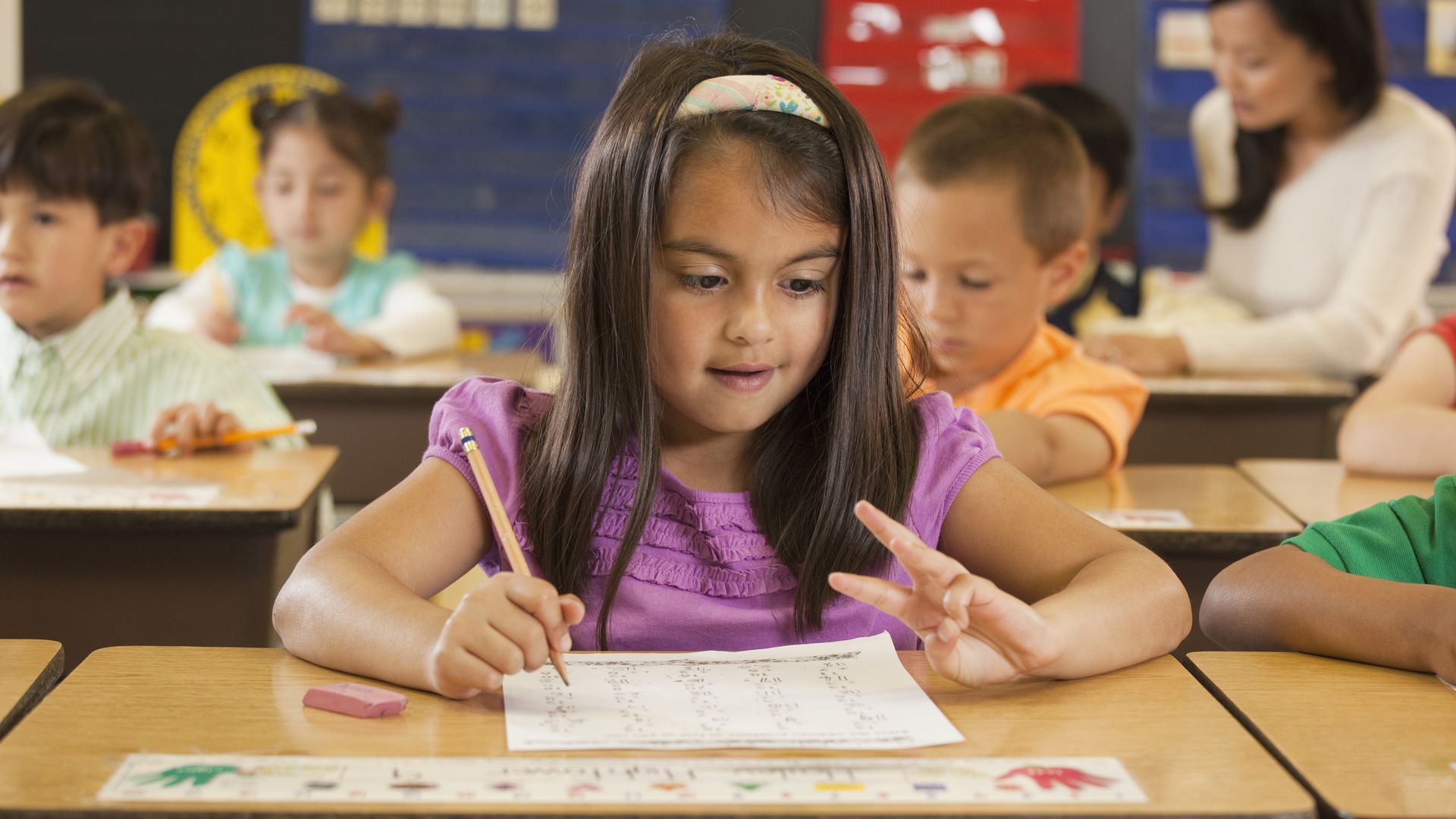 School girl at her desk counting on her fingers while doing math test