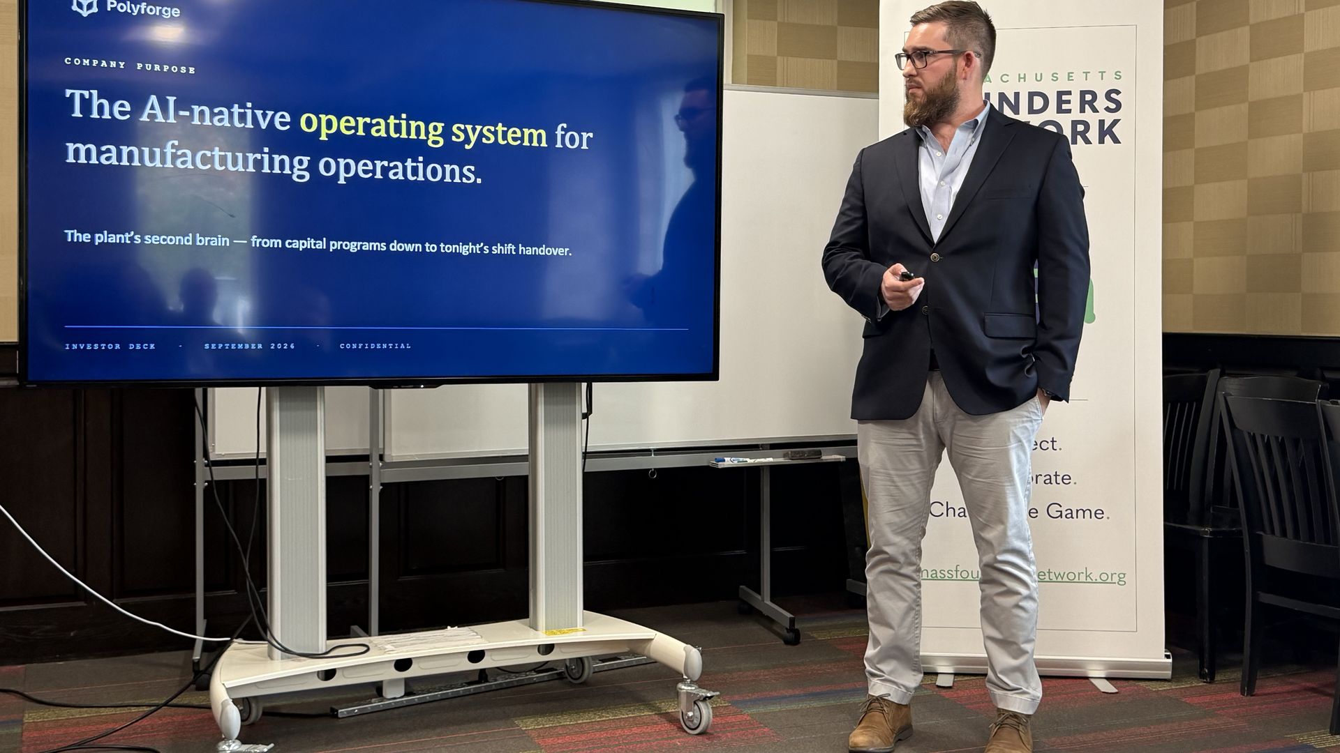 Jared Broberg stands next to the beginning of his slideshow in a university meeting room in Newton as he pitches his company, Polyforge.