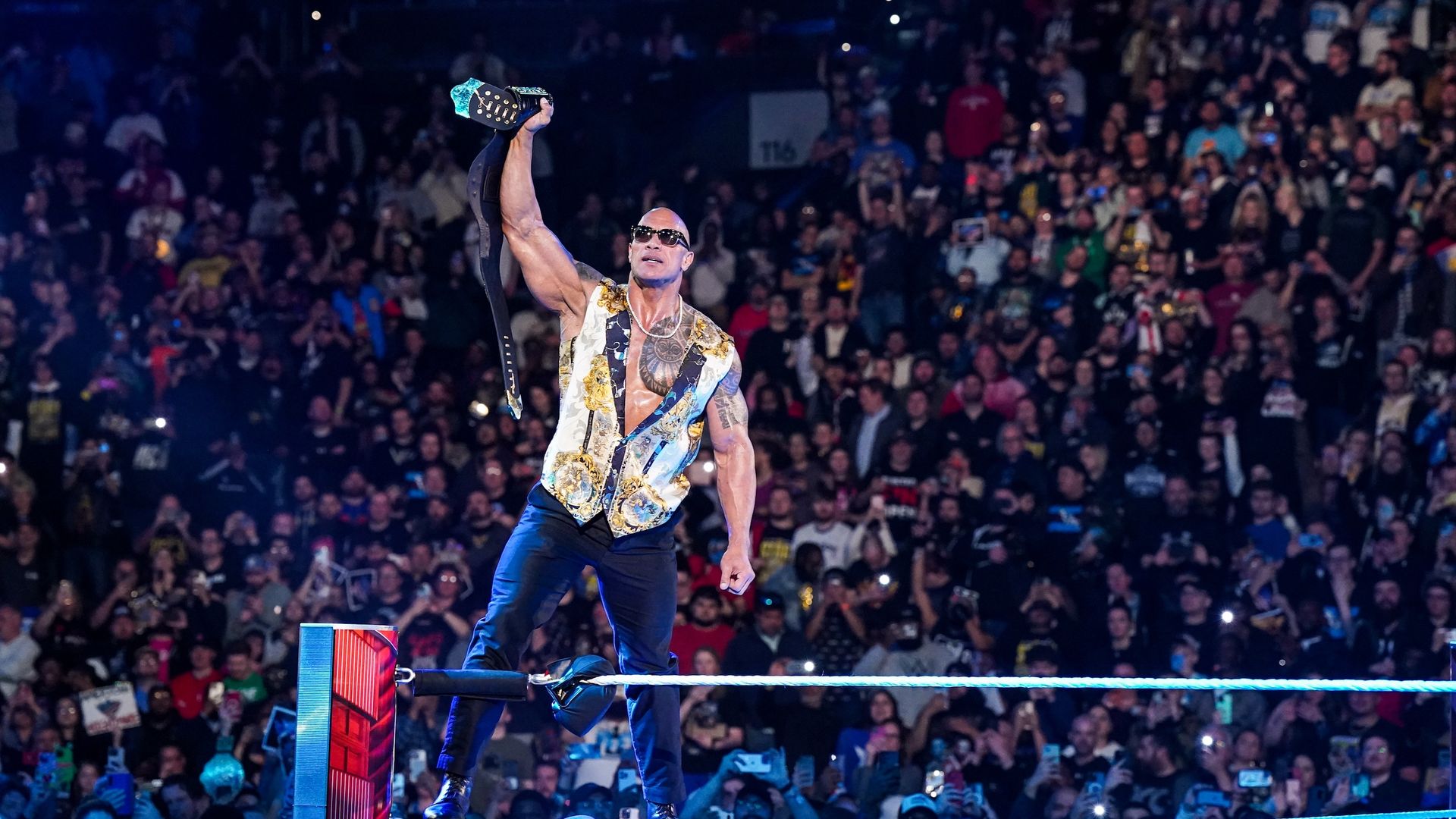 Dwayne "The Rock" Johnson holds up a championship belt at a WWE live event.