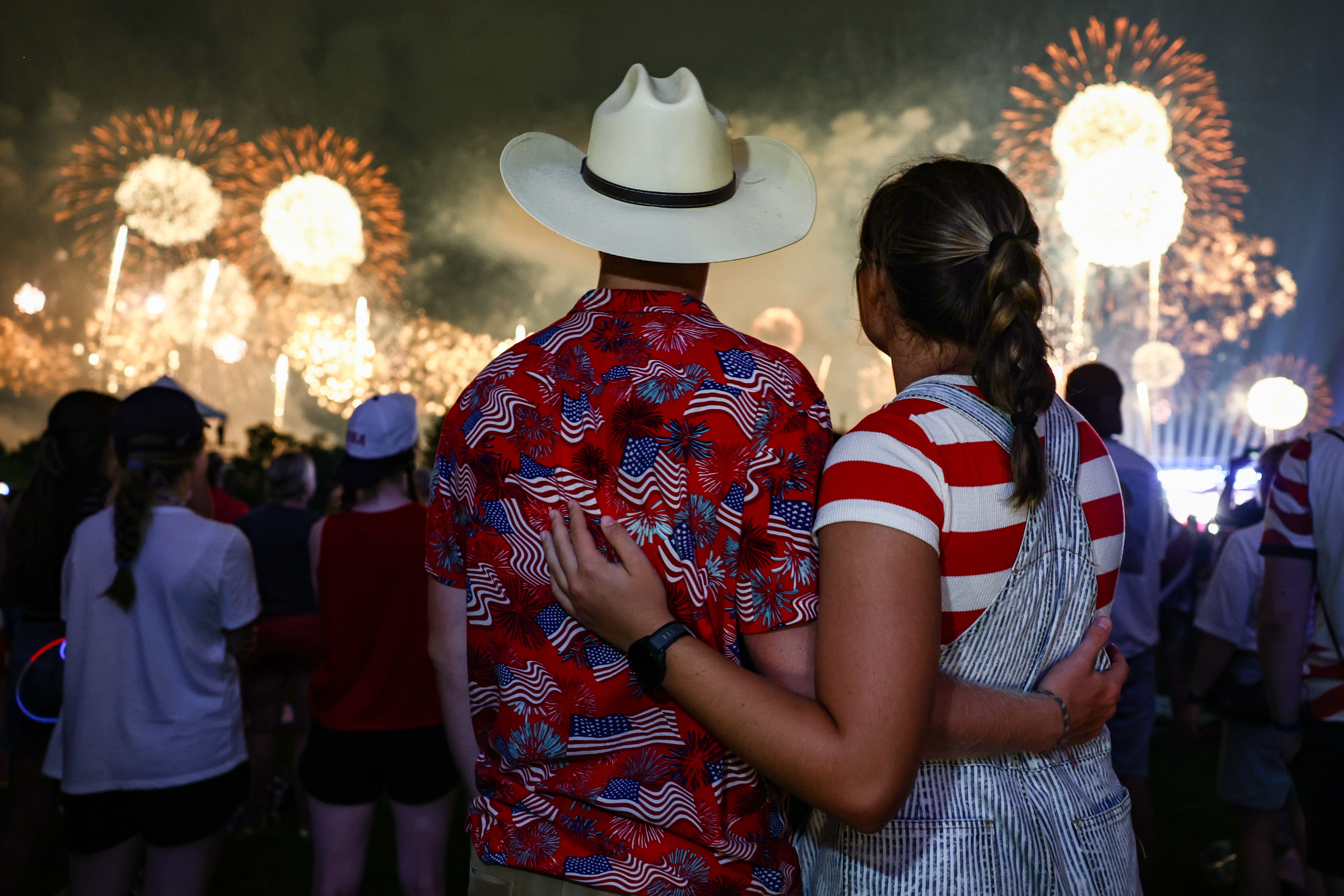 Two spectators, one wearing a white cowboy hat and the other with an arm around their companion, watch fireworks explode over the National Mall during the "Salute to America 250" Fourth of July celebration in Washington, D.C., on July 4, 2026.