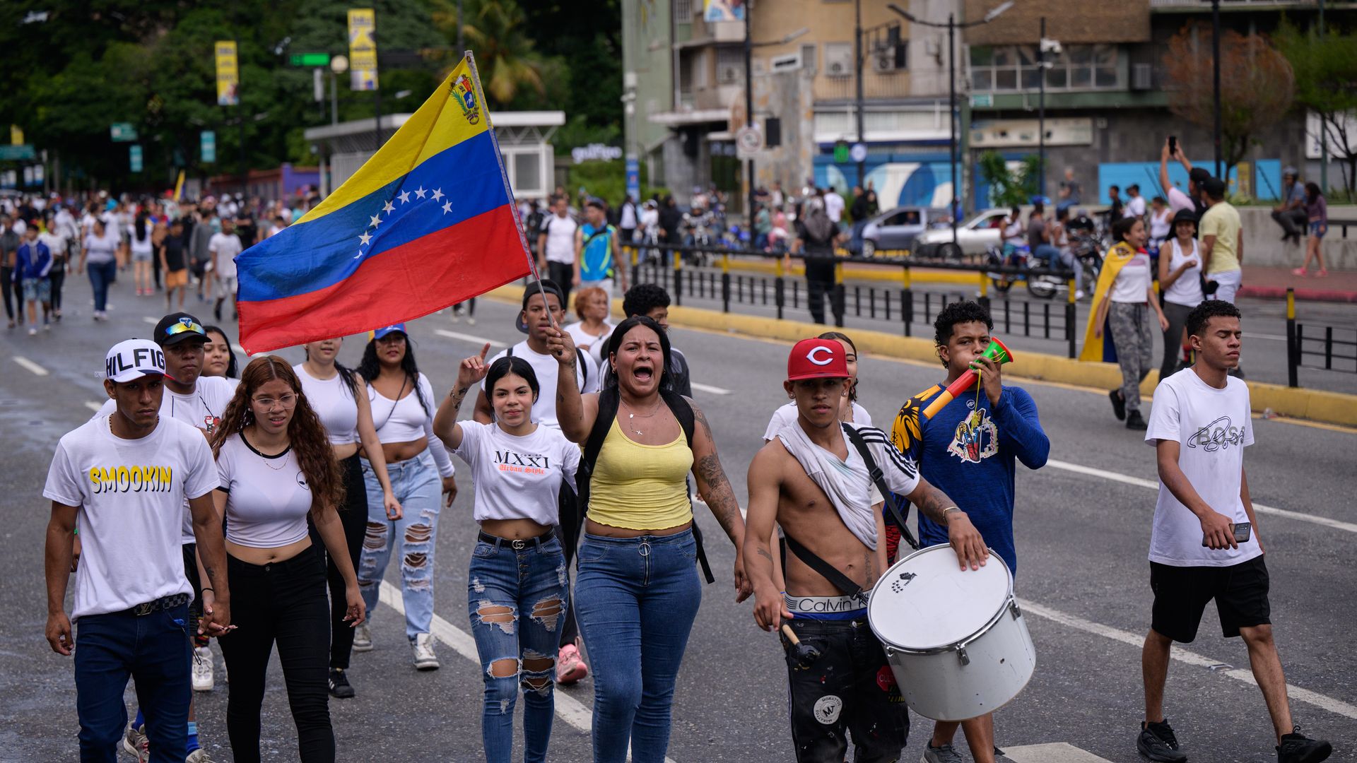Protesters march in Venezuela against President Nicolas Maduro. A woman holds a large Venezuela flag. 