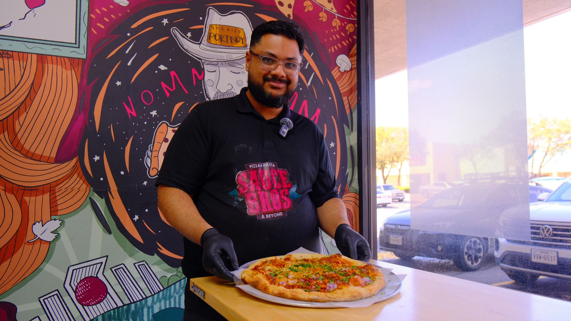 A man stands behind a table holding pizza