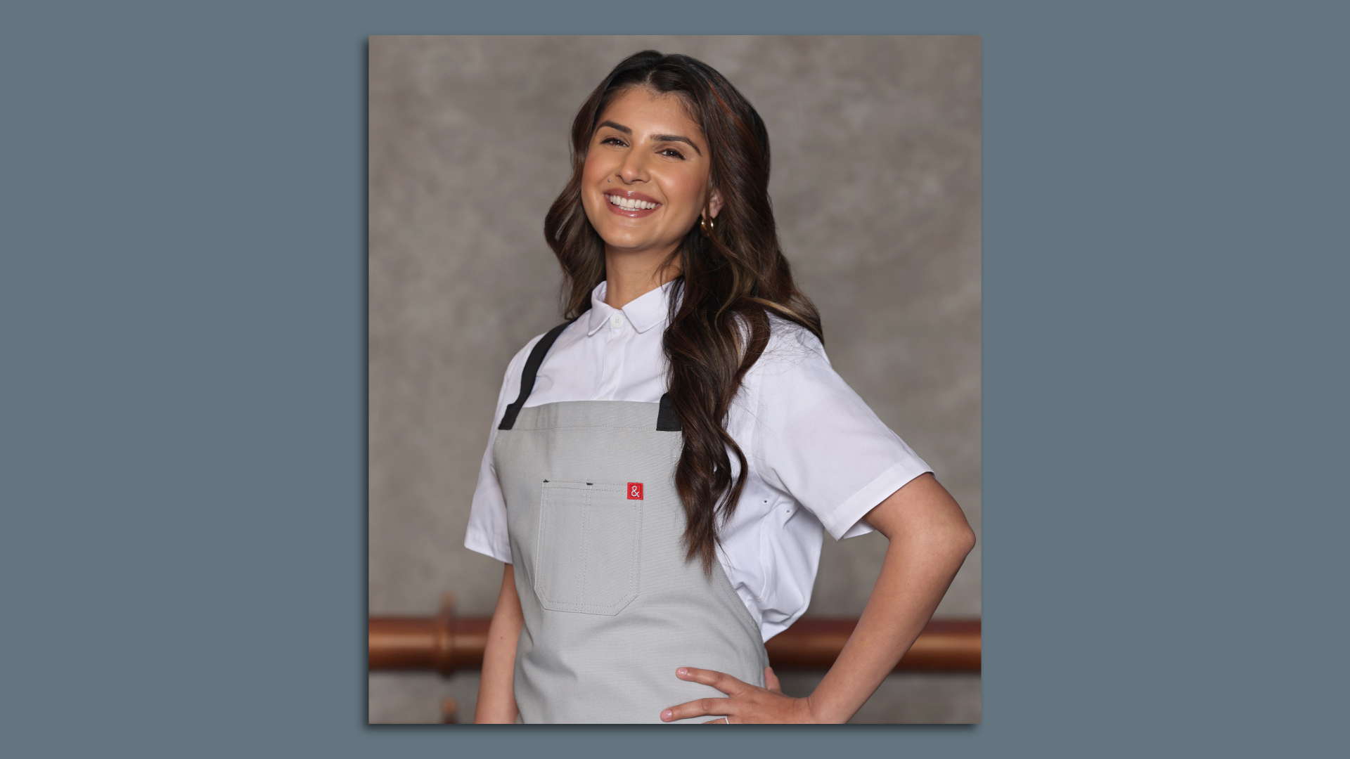 A woman wearing a gray apron stands with one hand on her hip