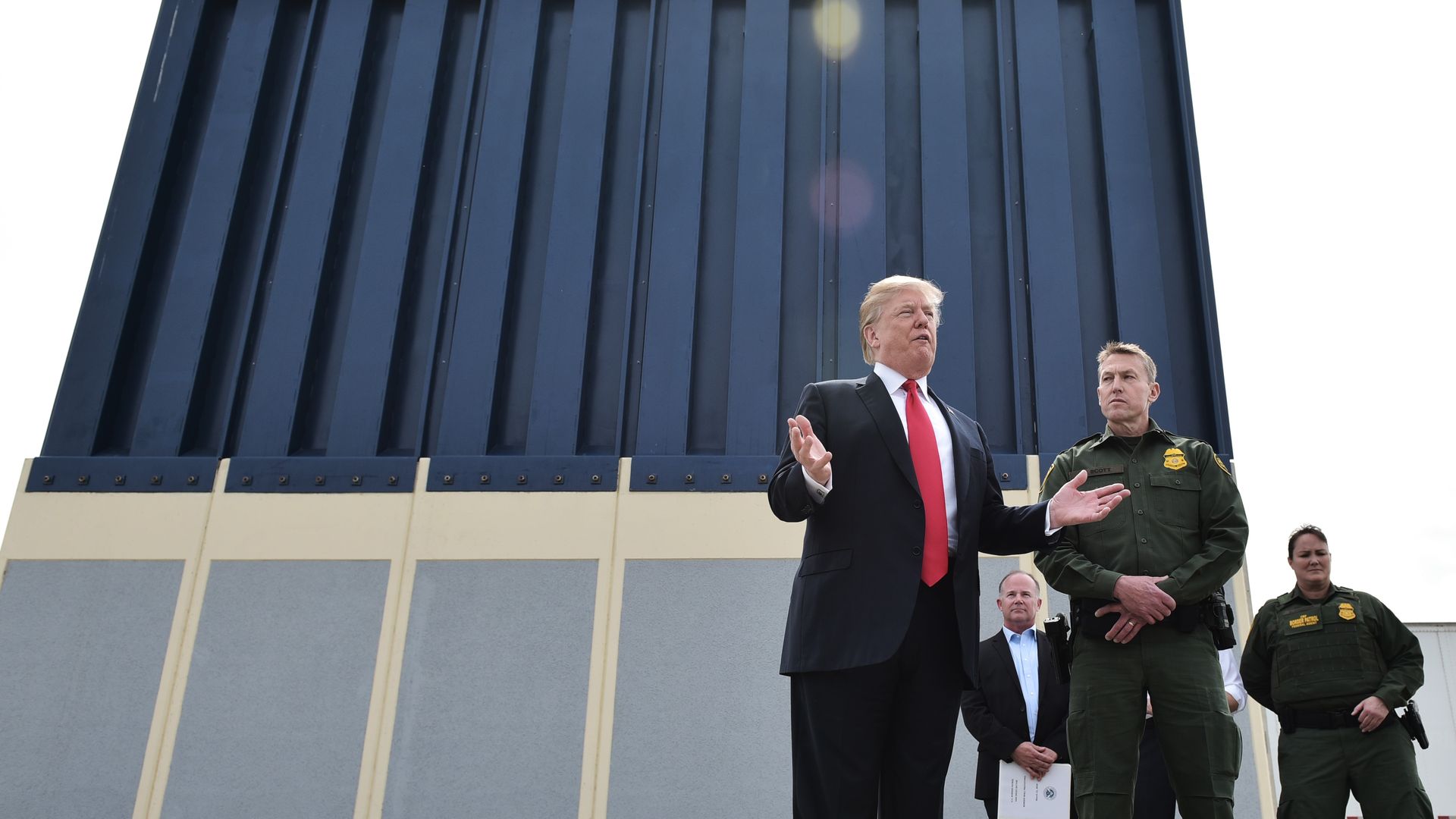 Trump stands in front of border wall prototype with law enforcement officers in green behind him