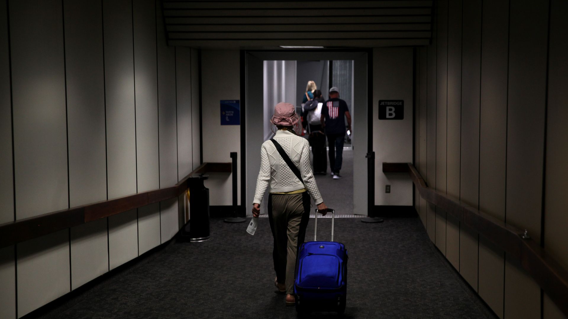 Photo of a passenger rolling a blue suitcase captured from behind