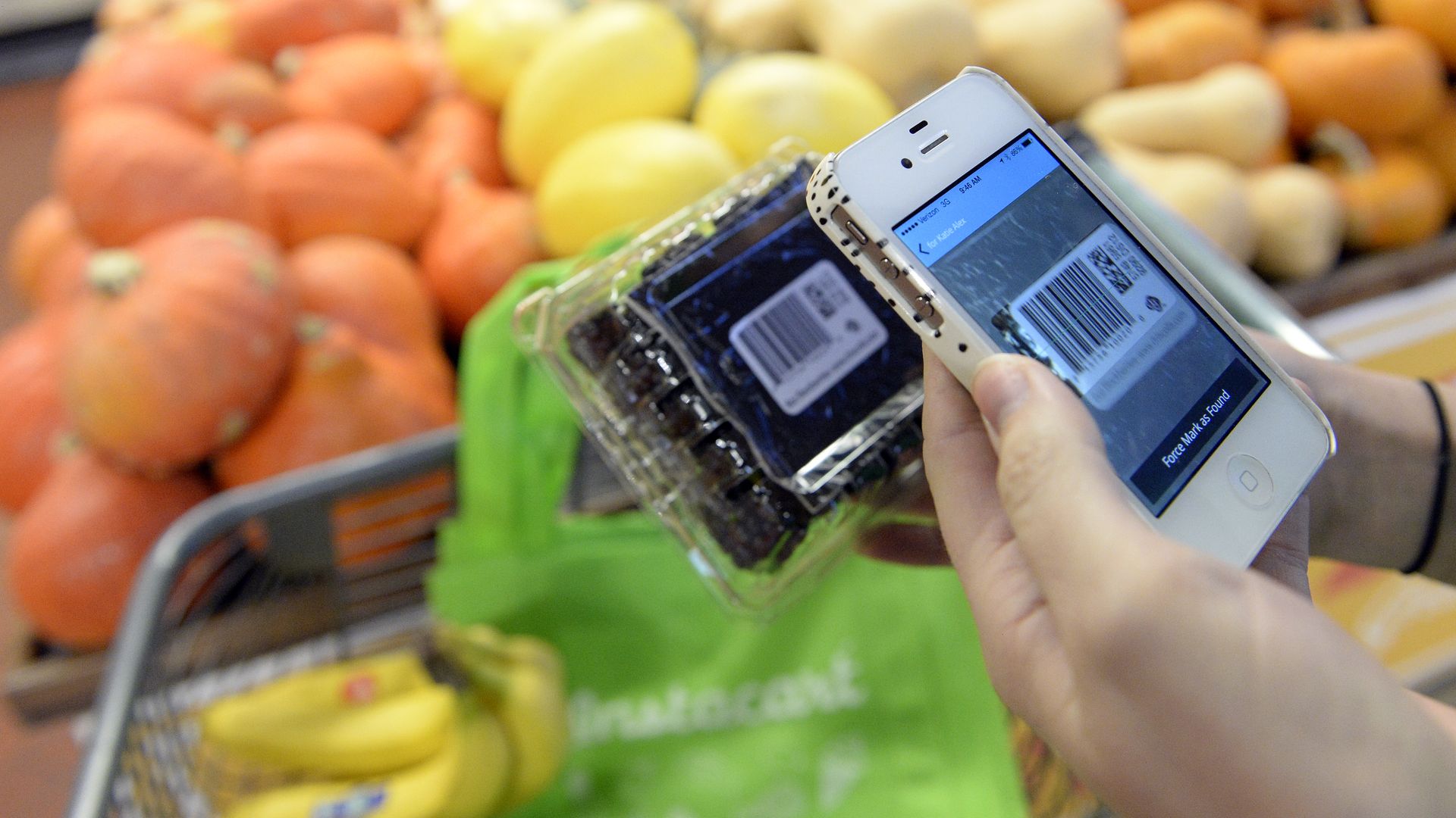 Photo of Instacart shopper phone scanning blueberries and a cart with groceries.