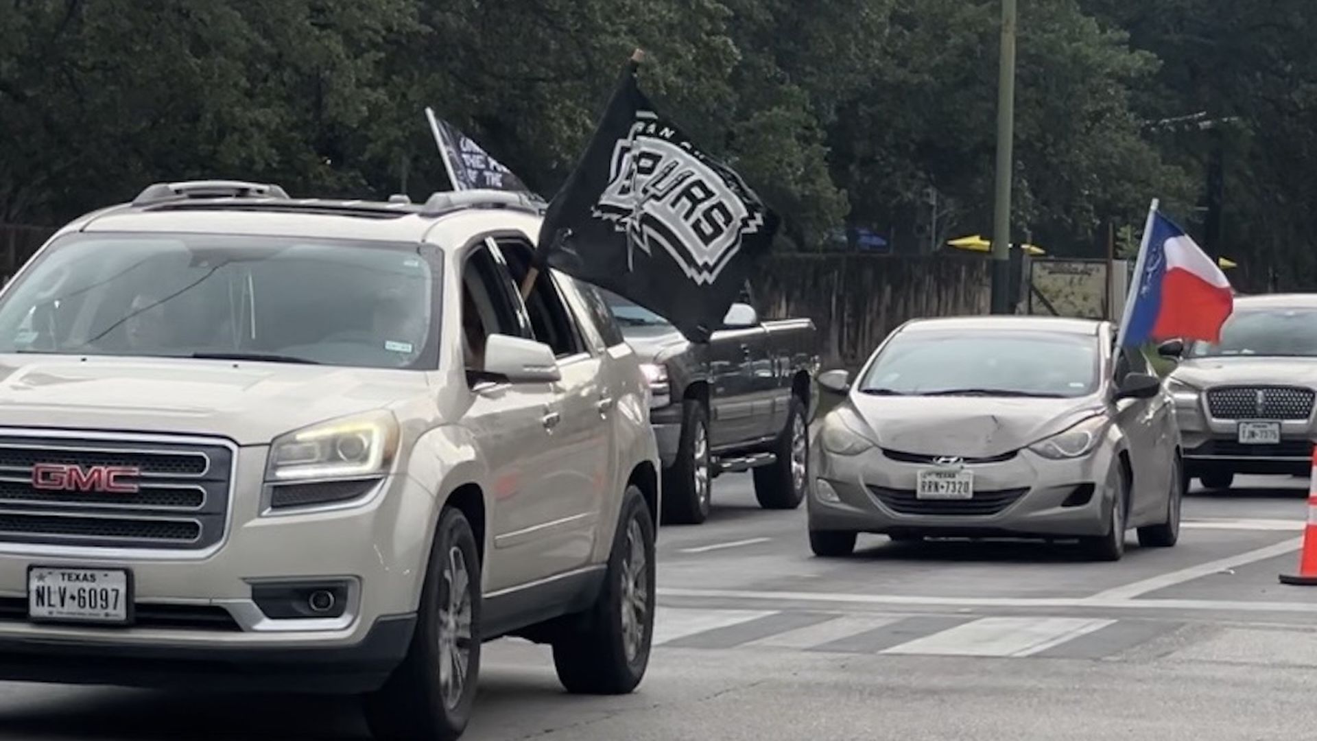 Fans waving Spurs flags drive down a crowded street. 