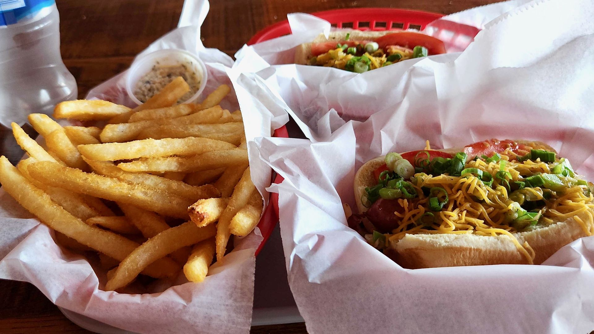 A close-up of a loaded hot dog and fries in red plastic baskets lined with white paper