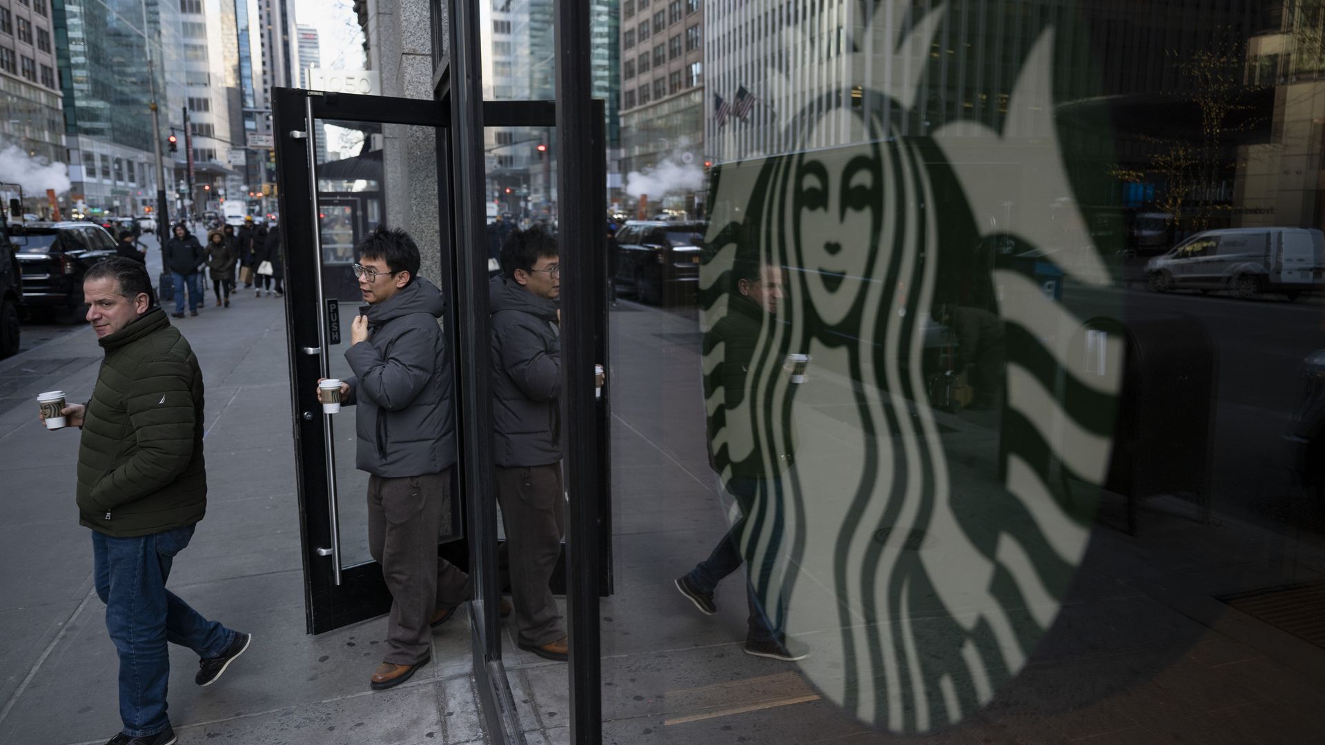 People exit a Starbucks store holding cups of coffee.