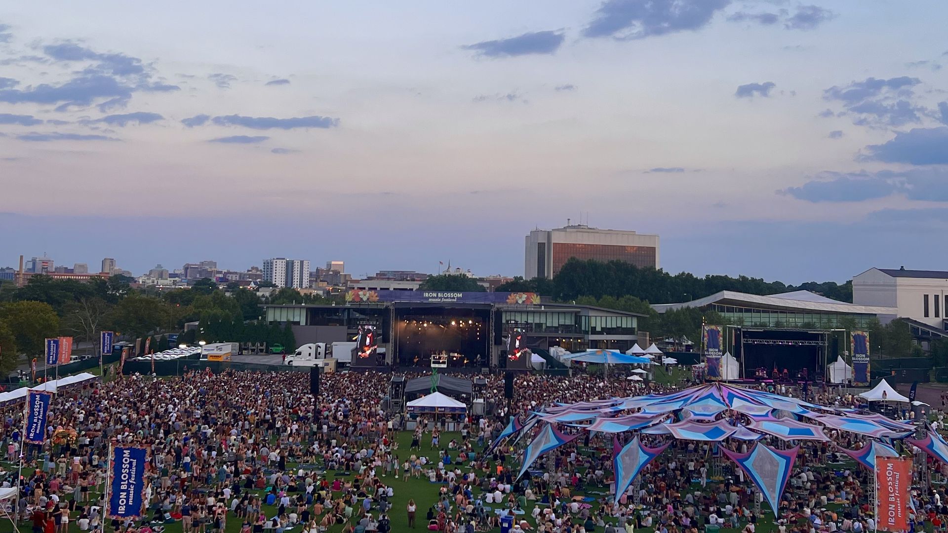 A picture from high up of a crowd at a festival with the sunset and Richmond skyline in the background.