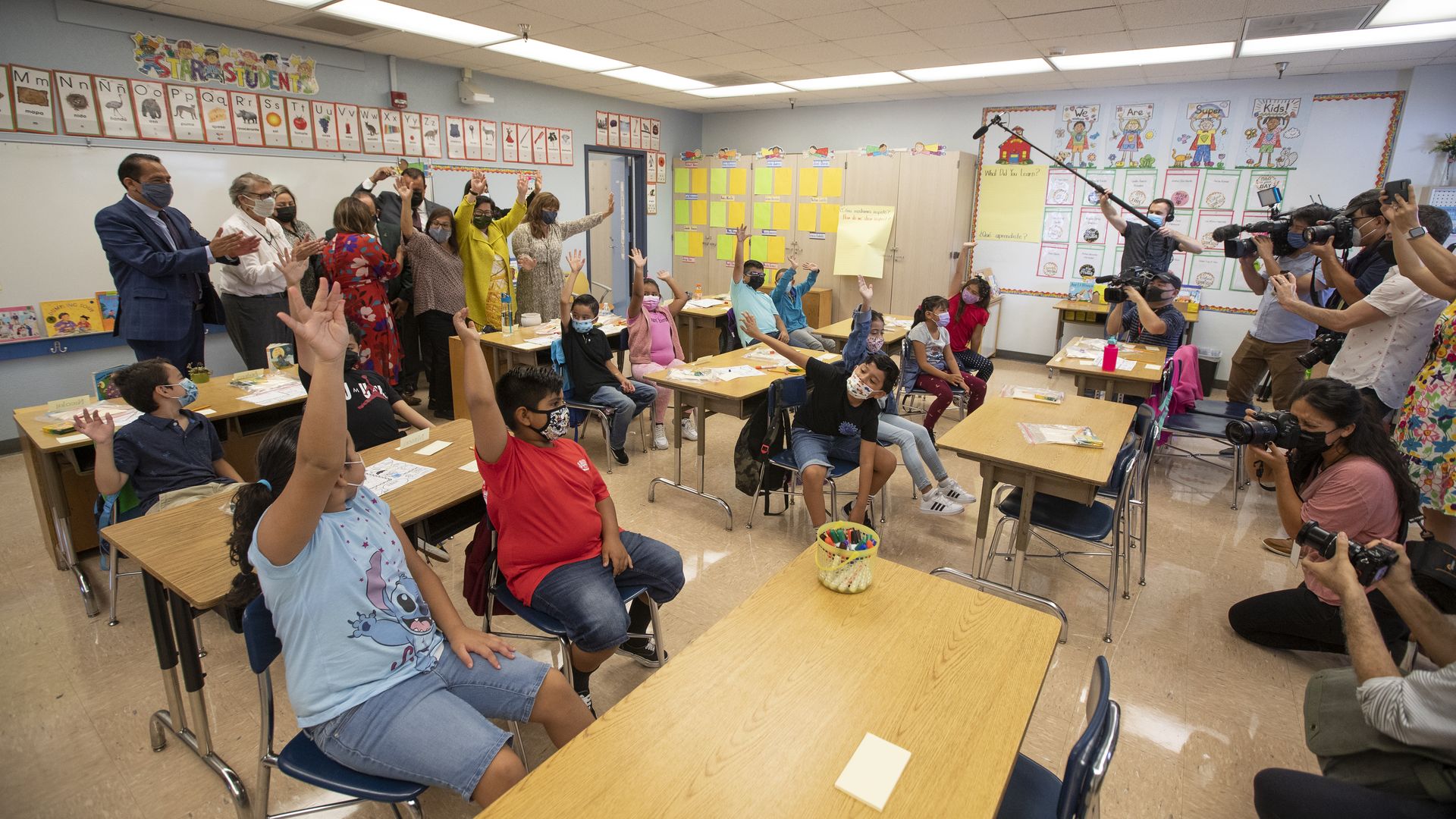 Photo of children sitting in a classroom raising their hands