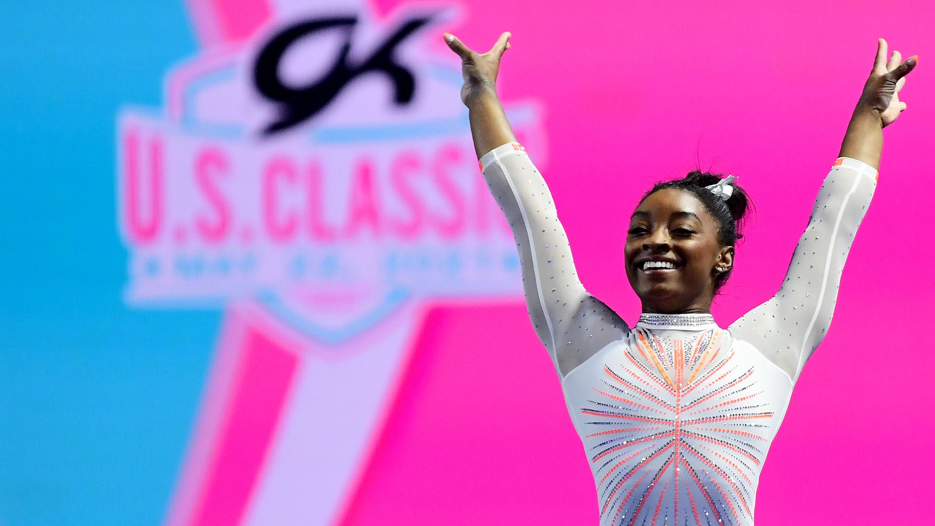 Photo of Simone Biles smiling with her arms raised high into the air at the U.S. Classic gymnastics competition