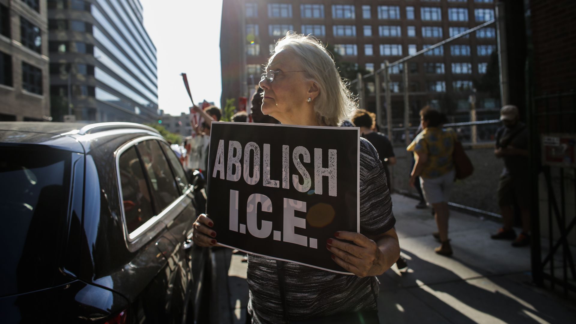 A woman holds a sign in protest, reading "Abolish I.C.E."