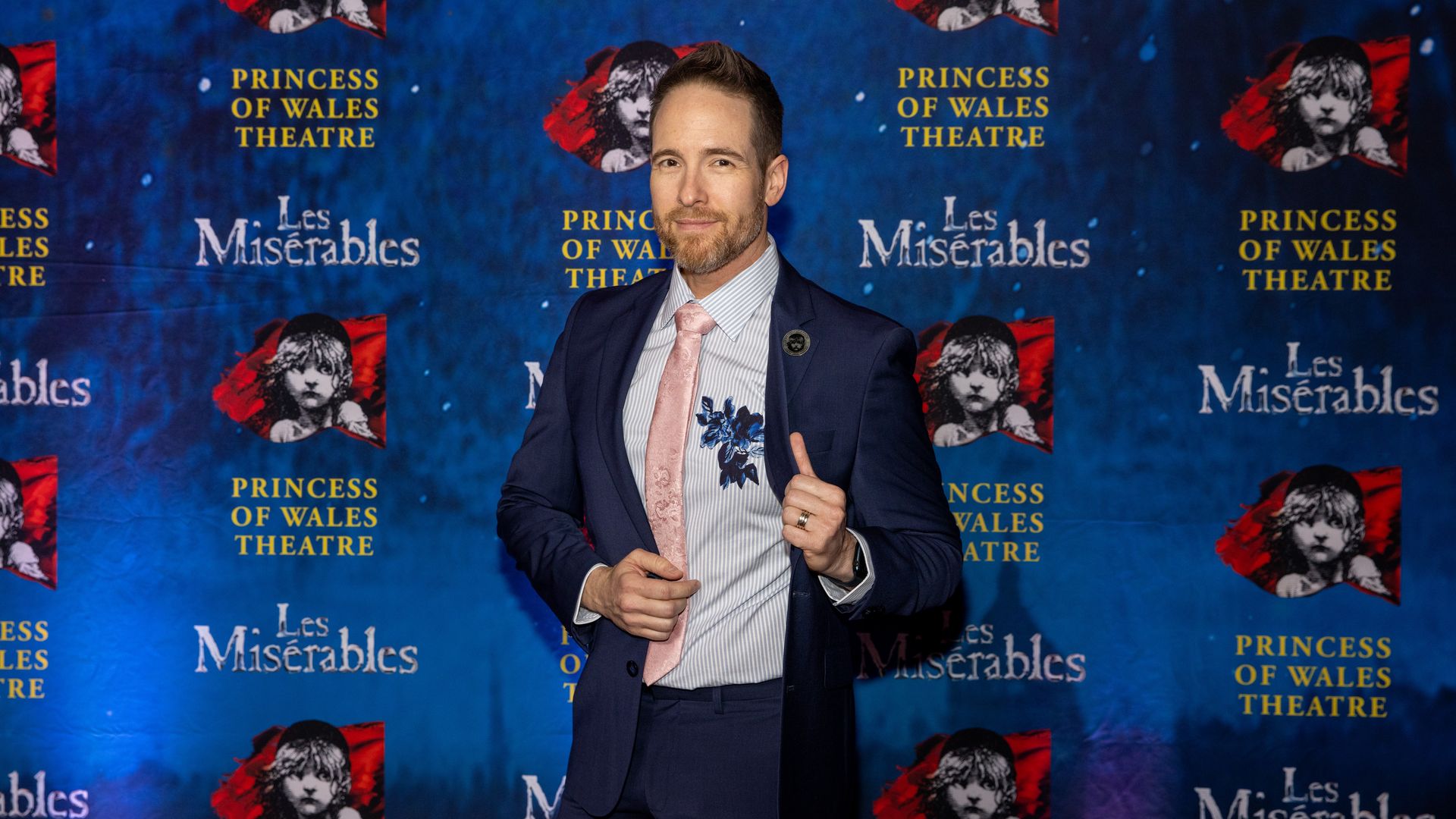 A man smiling in front of a Les Miserables poster.