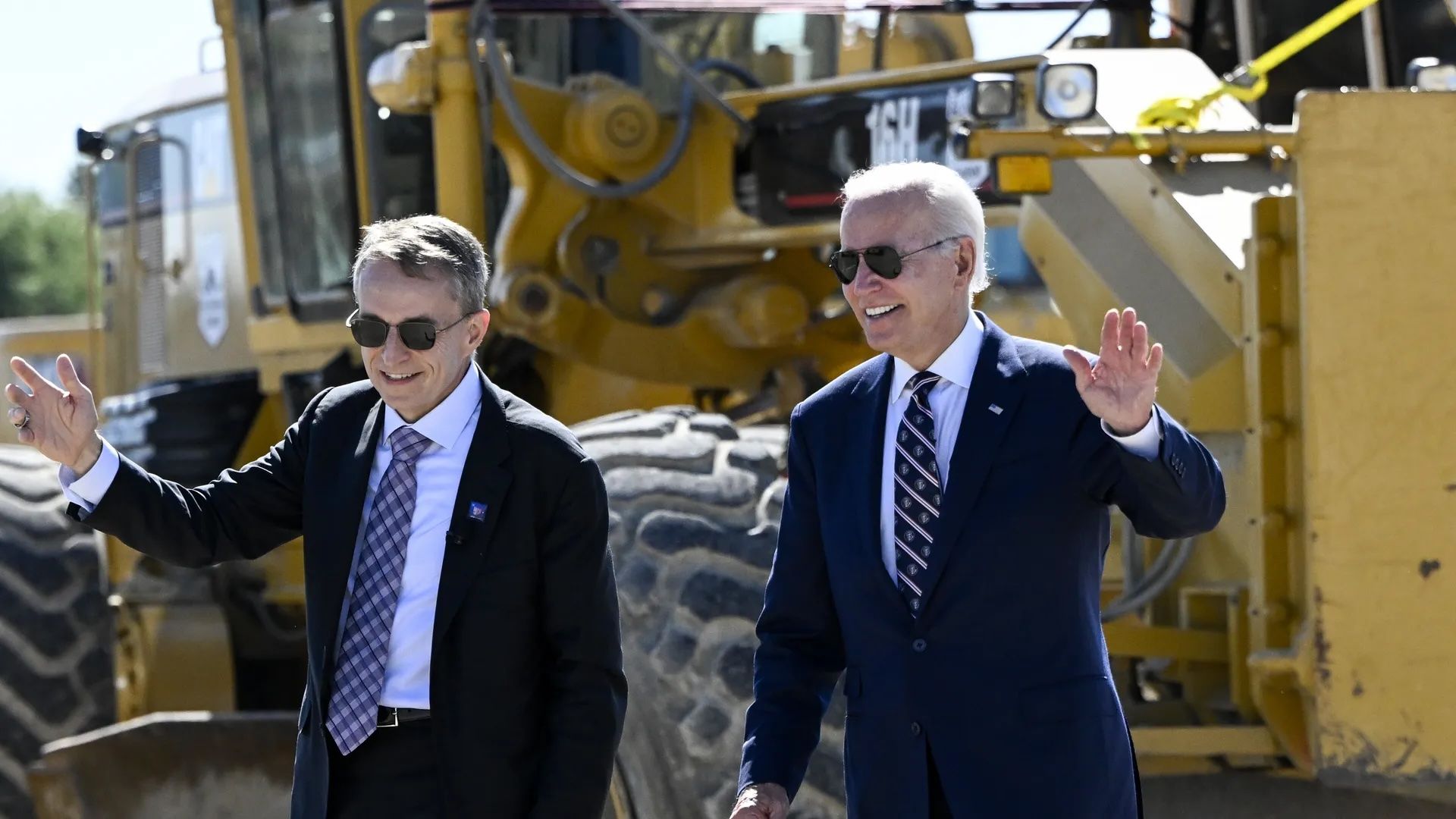 President Biden and another man waving in front of construction equipment. 