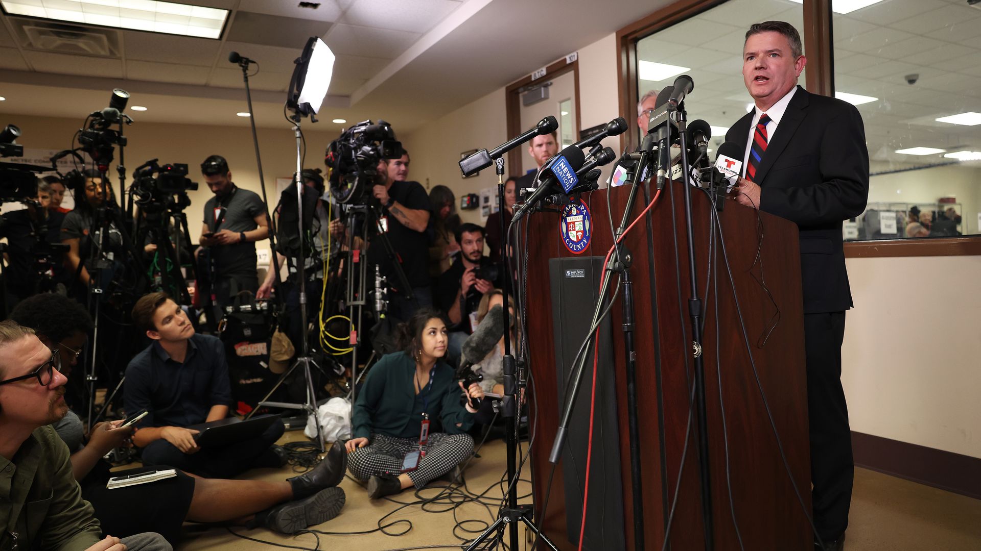 A man speaks at a podium in front of cameras.