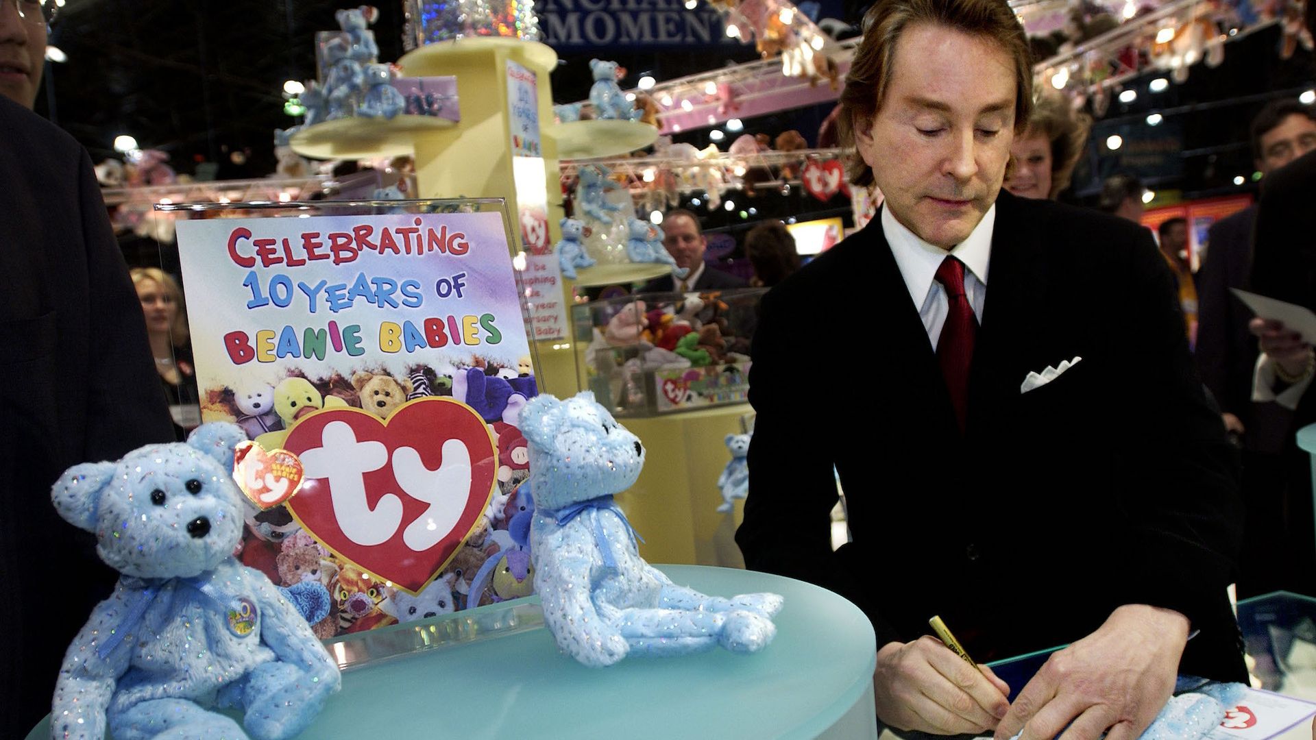 Photo of a man signing autographs next to stuffed animals 