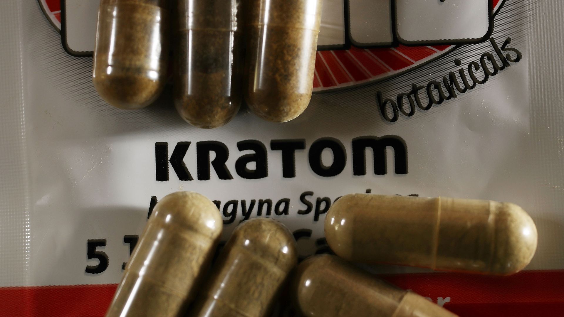 Close-up of clear capsules filled with brownish powder on a white and red package labeled "KRATOM botanicals".