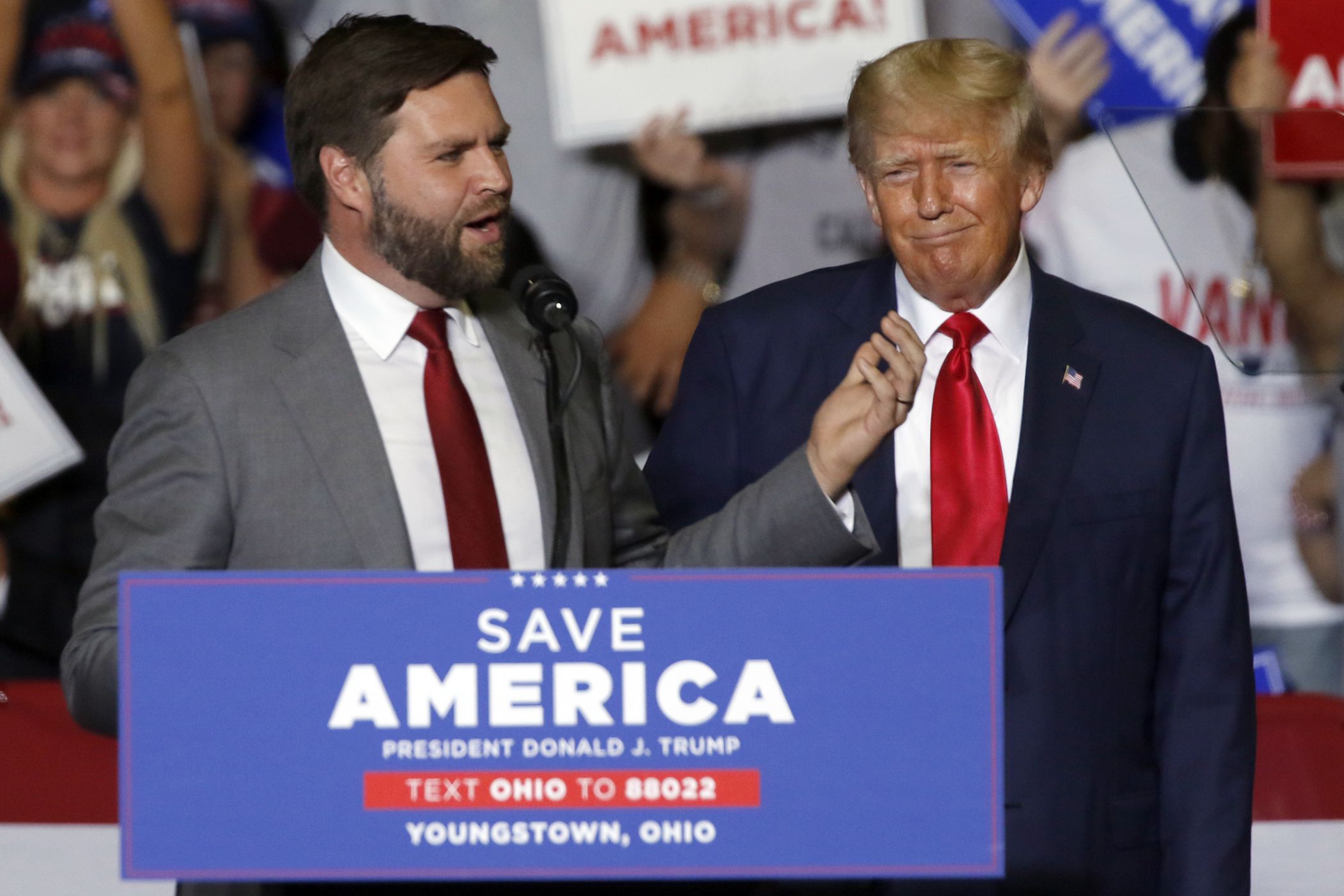 J.D. Vance and Donald Trump stand behind a podium that says "Save America," with Vance speaking