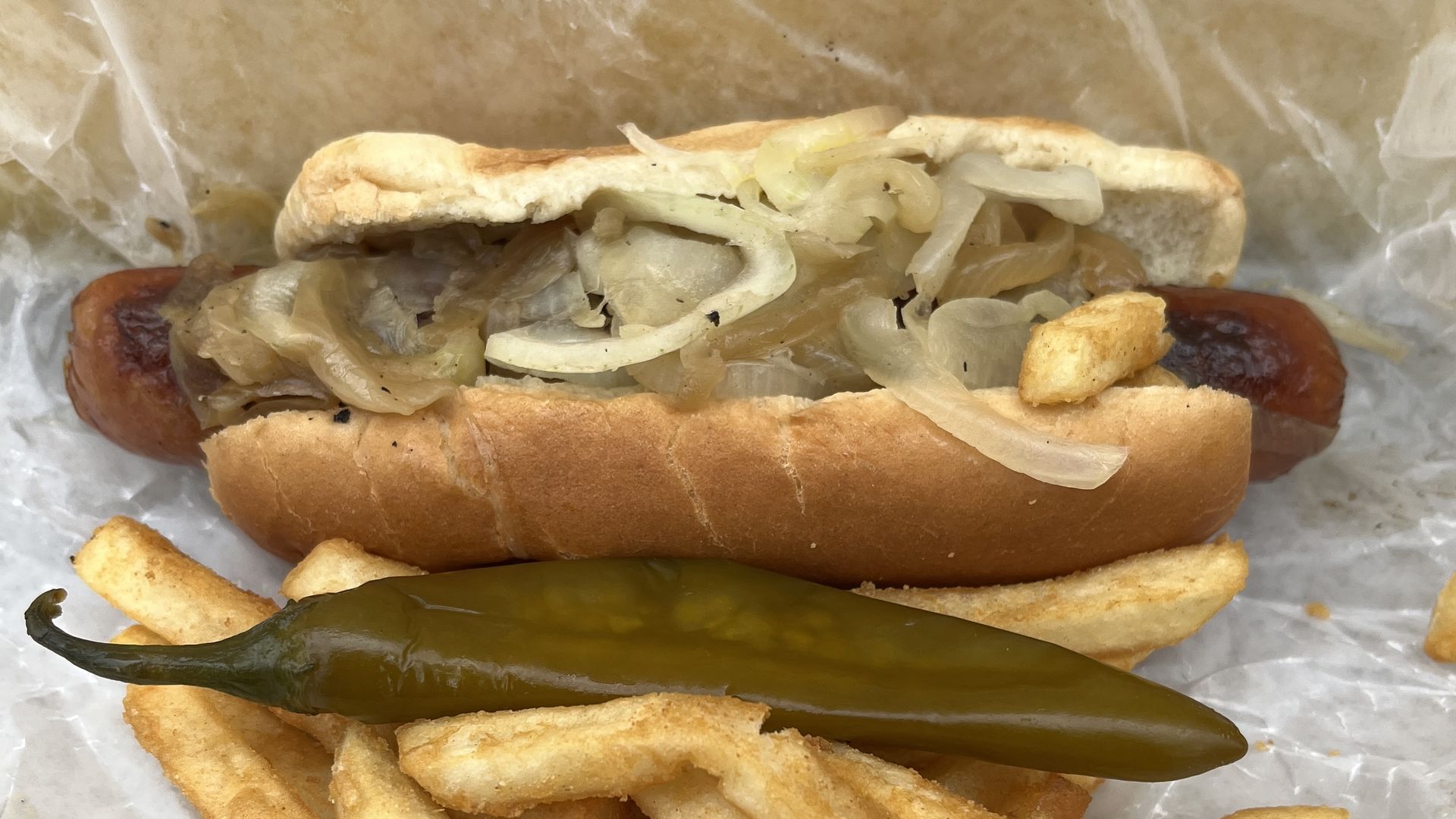 Sausage in a bun wth a pepper and fries 