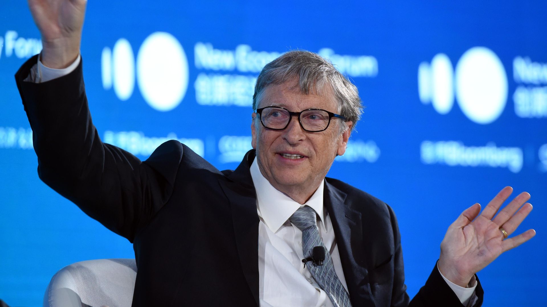 In this image, Bill Gates sits and talks while waving his arms