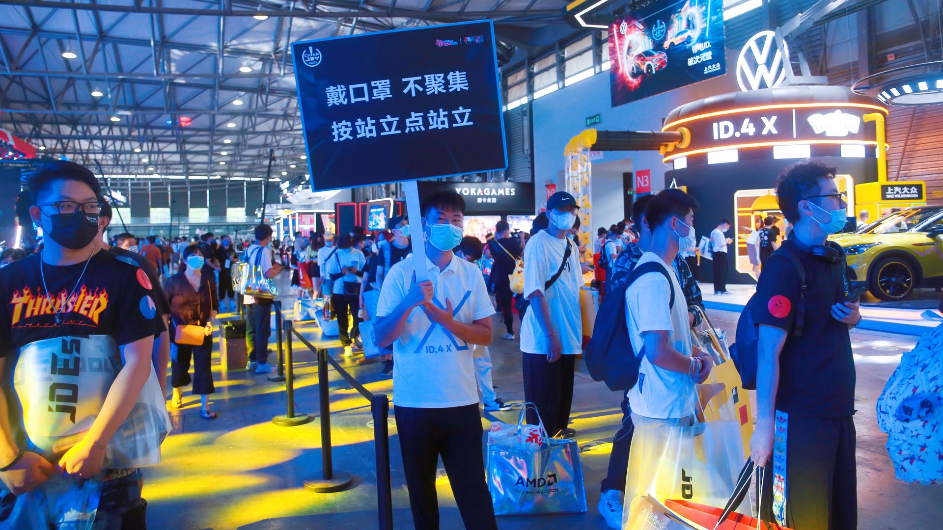 People at a gaming convention in China. A man holds a sign telling people to practice social distancing.