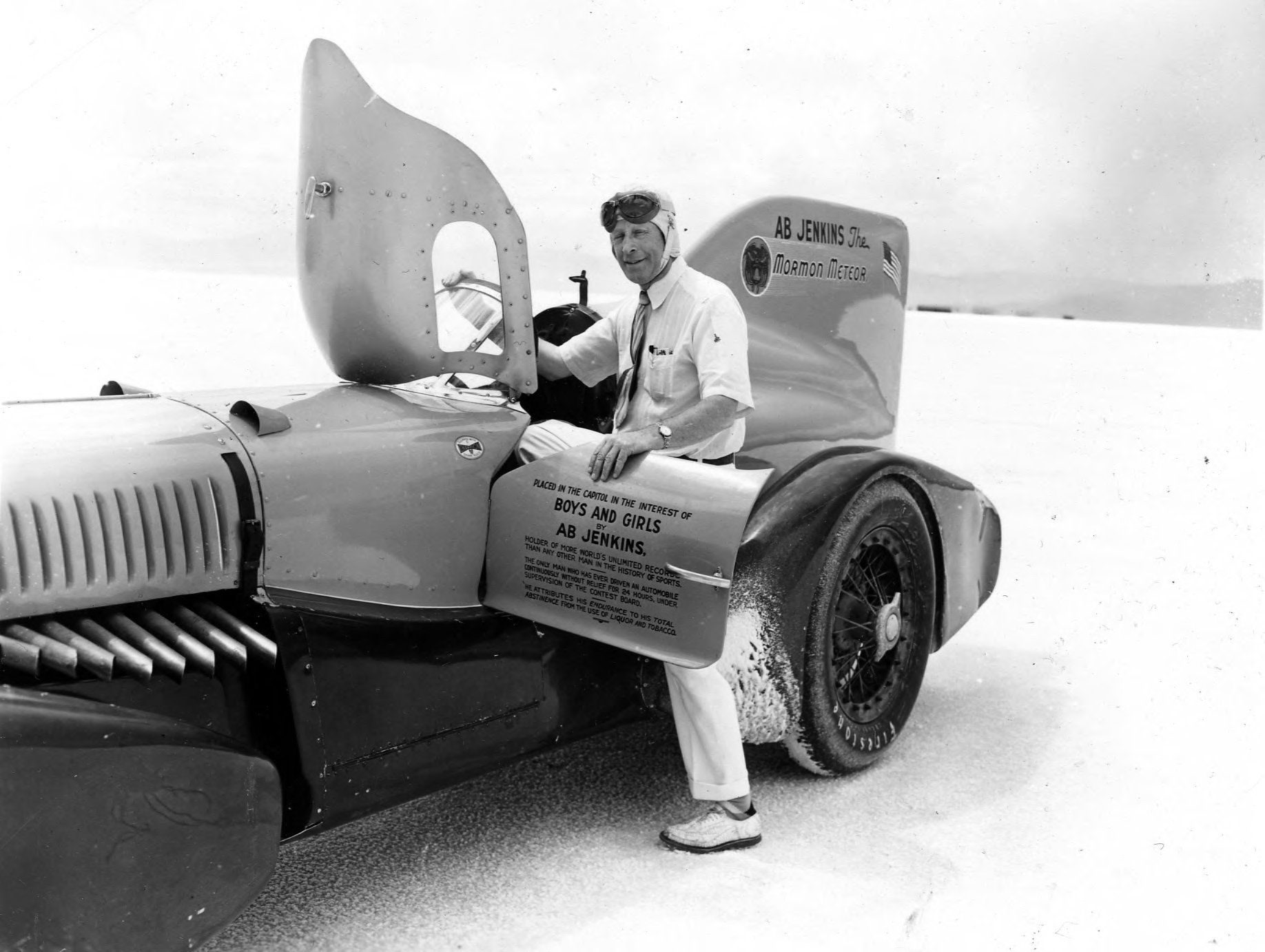 Old photo of a 1930s race car, with a driver opening the door and top hatch