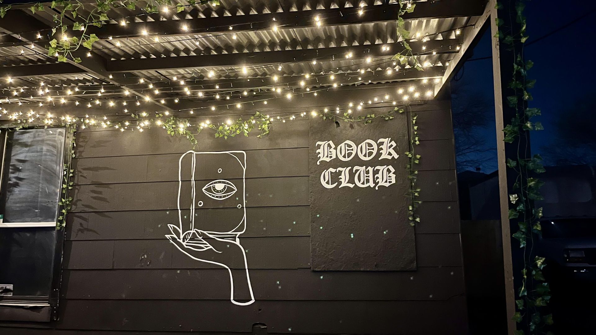 An all-black building is adorned with a white image of a hand holding a book with an eyeball on it and the text "Book Club."