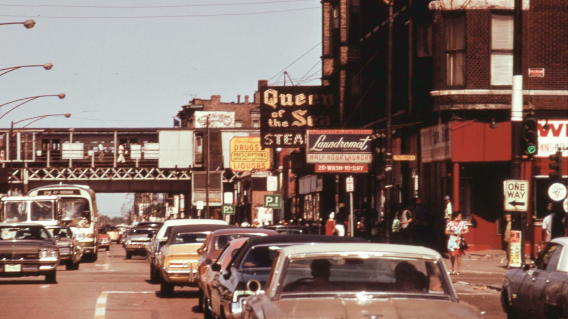 An archive photo of a street with old signs and a train station in the background. 
