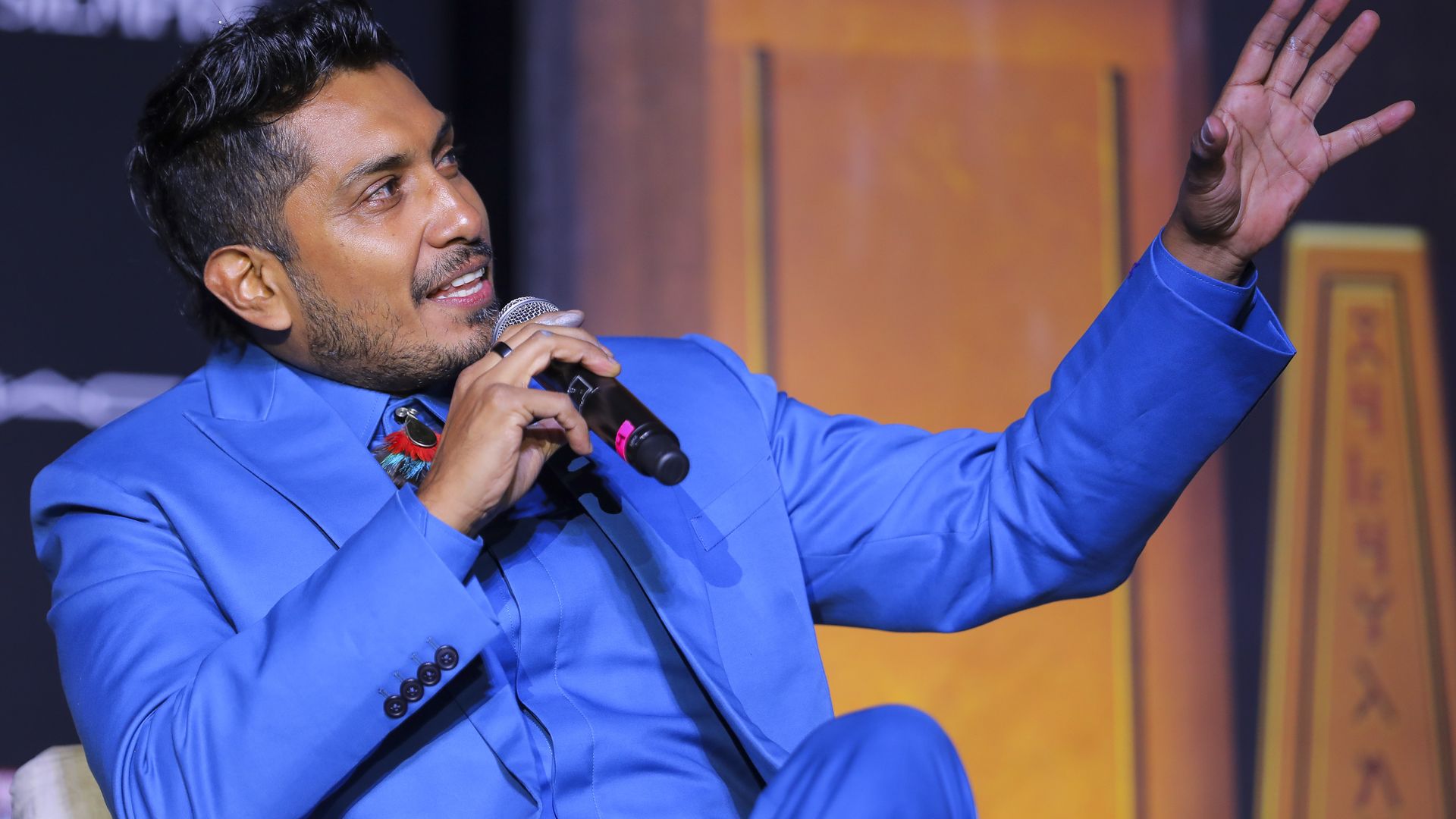 Actor Tenoch Huerta sits on a couch, holds a microphone to his face and looks off to the side during a press event in Mexico City