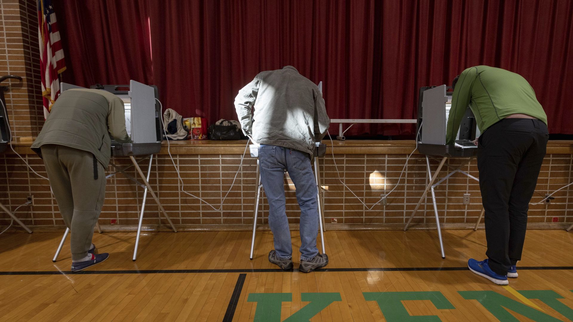 Three voters cast ballots in the gymnasium of an elementary school in Minneapolis.
