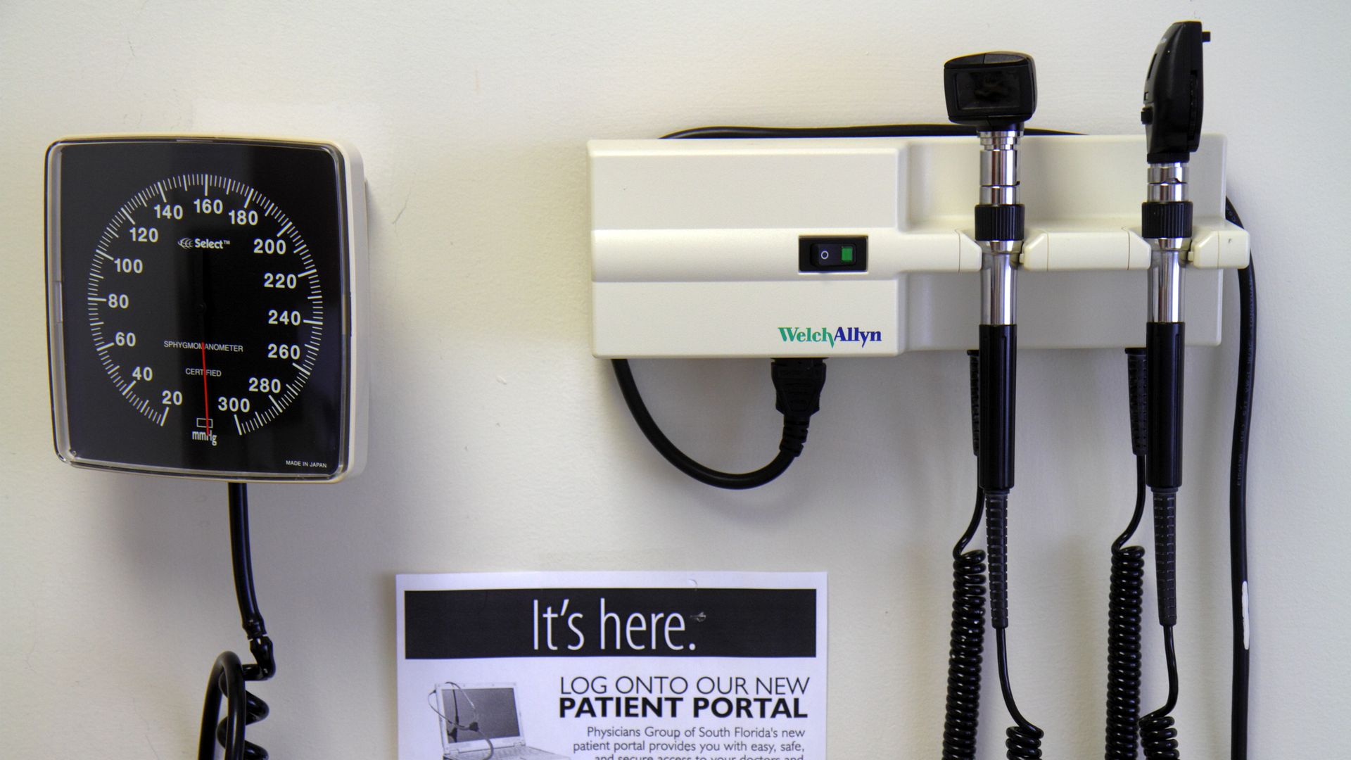 A blood pressure cuff, eye light, and ear tool hang on a wall in a doctor's office.