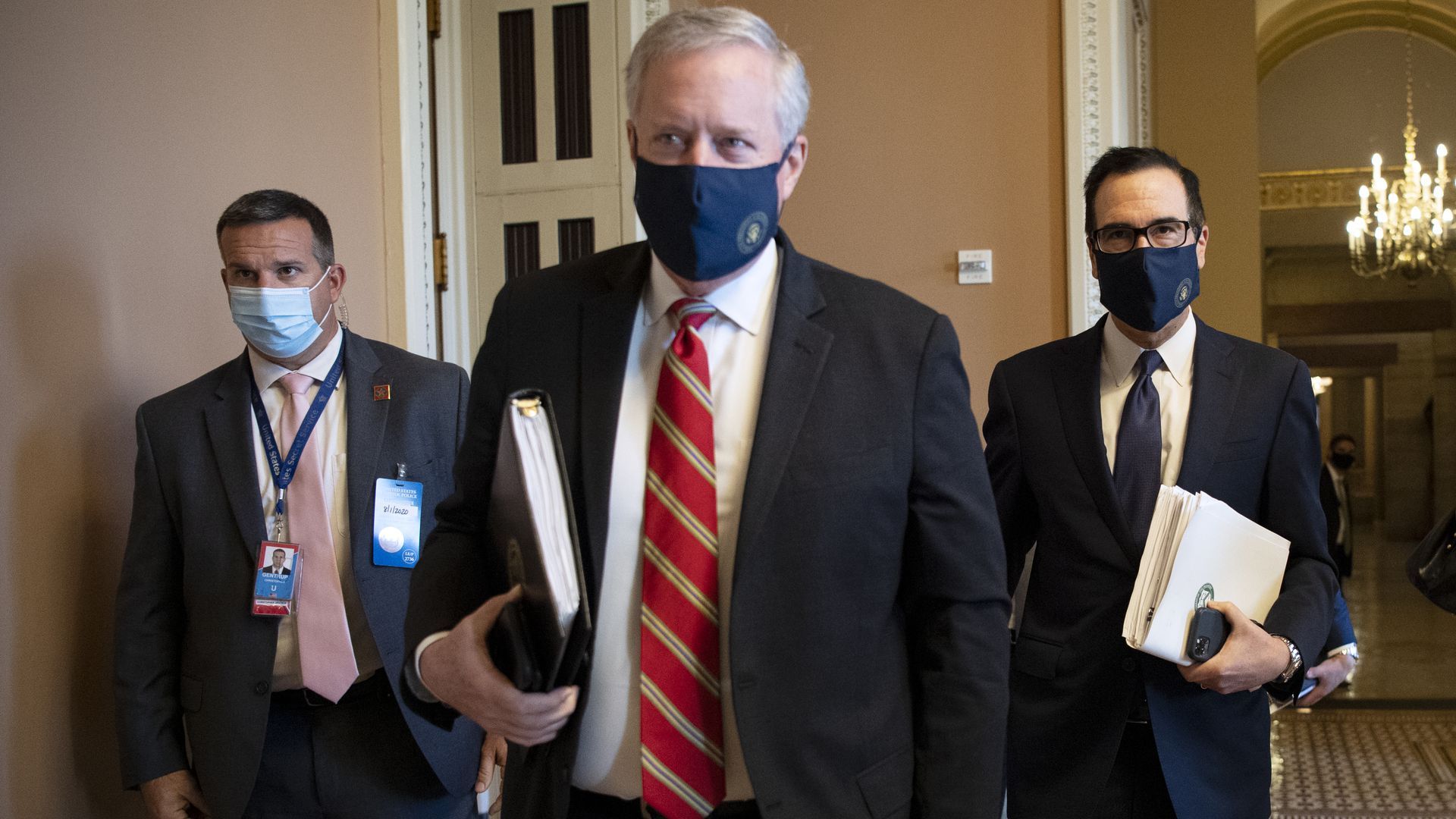 Mark Meadows, Steven Mnuchin walk down a hall wearing suits and face masks