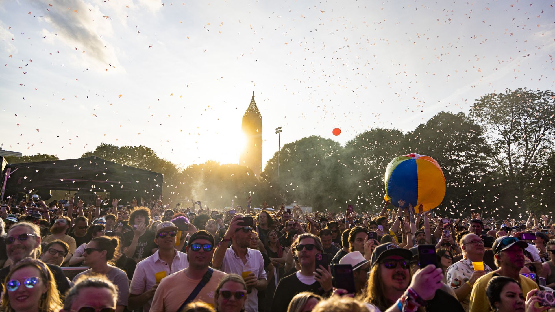 The sun sets behind the Atlanta skyline as a crowd at an outdoor concert dances and bounces a big ball overhead