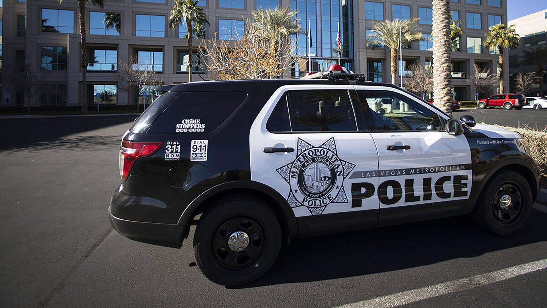 Black and white Las Vegas Metropolitan Police SUV parked in front of a modern building with palm trees and clear blue sky.