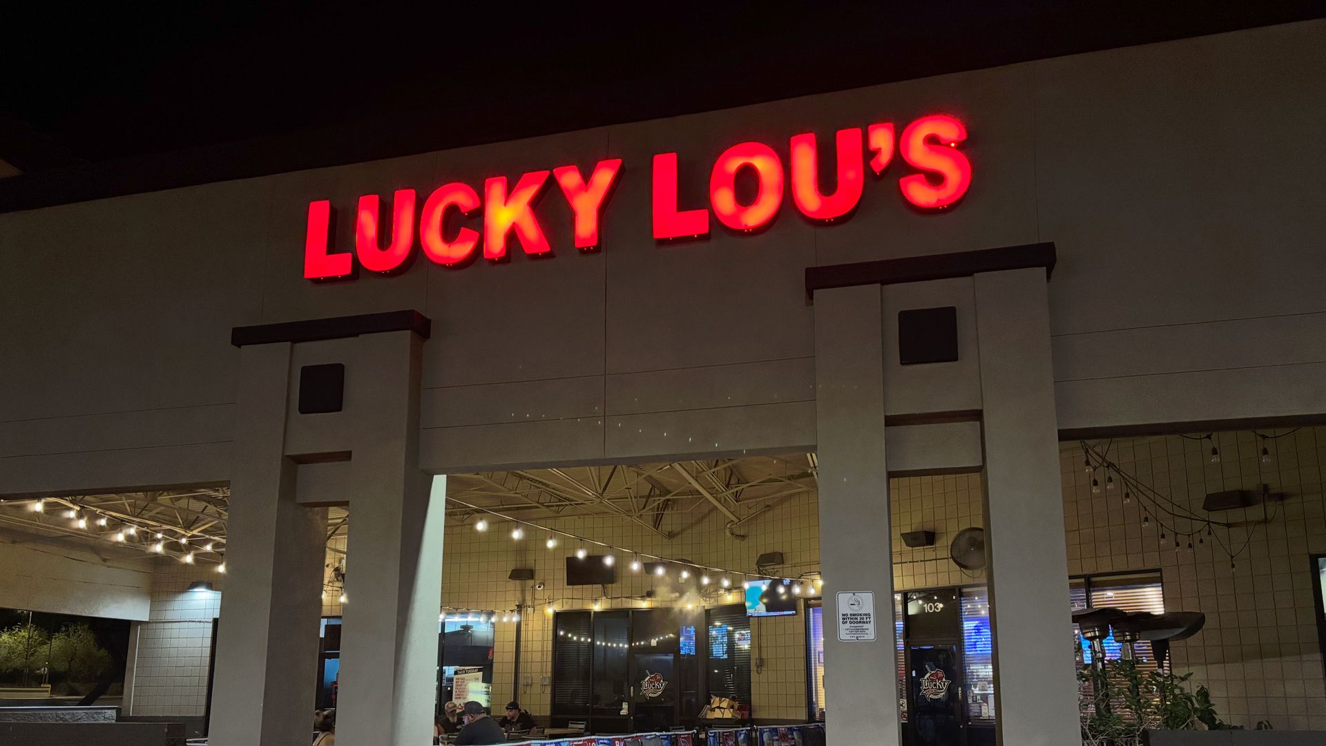 The exterior of a building with a neon red sign that reads "Lucky Lou's"