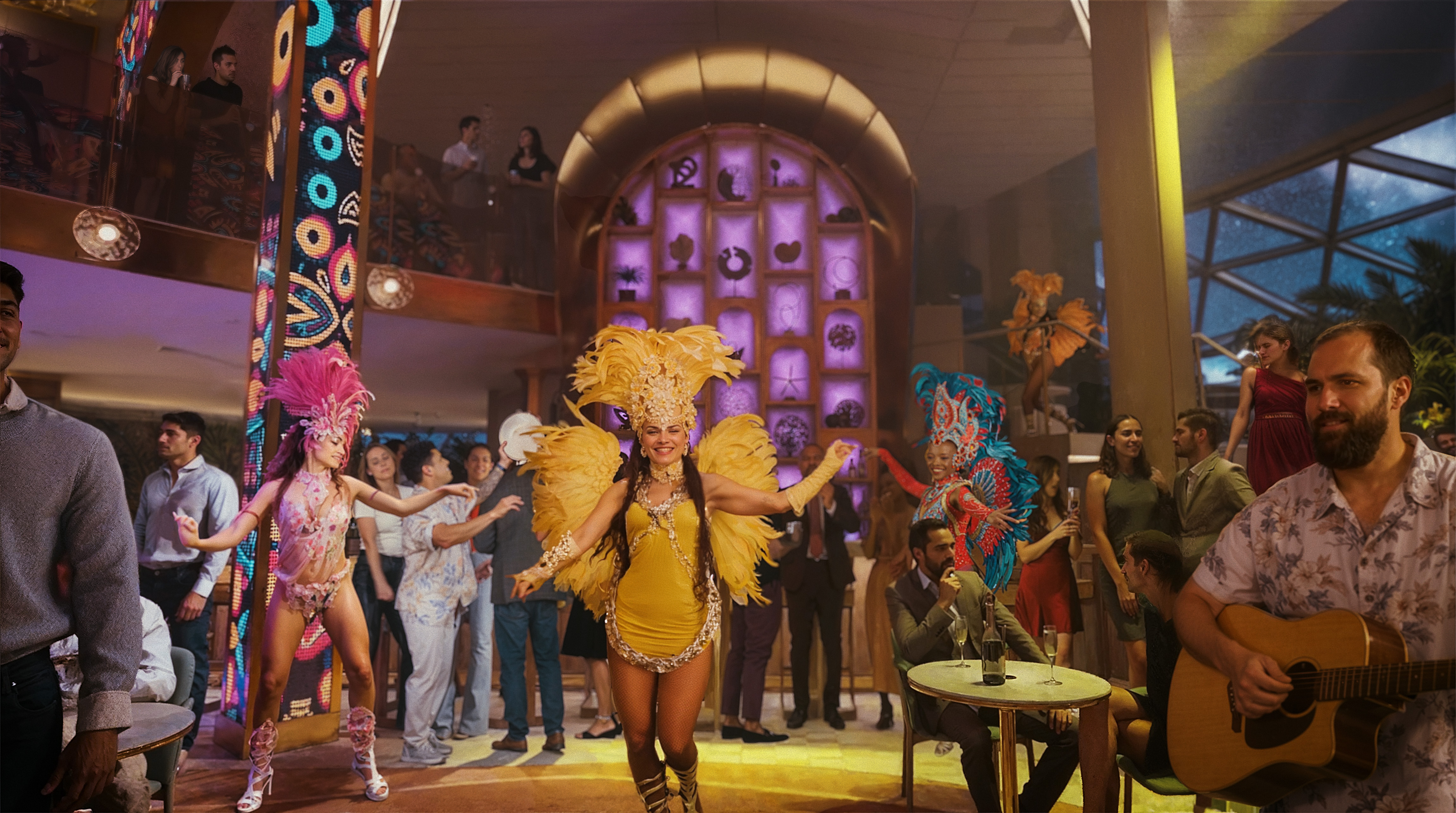 A lively indoor party with colorful feathered dancers in yellow, pink, and blue costumes performing amid a crowd.