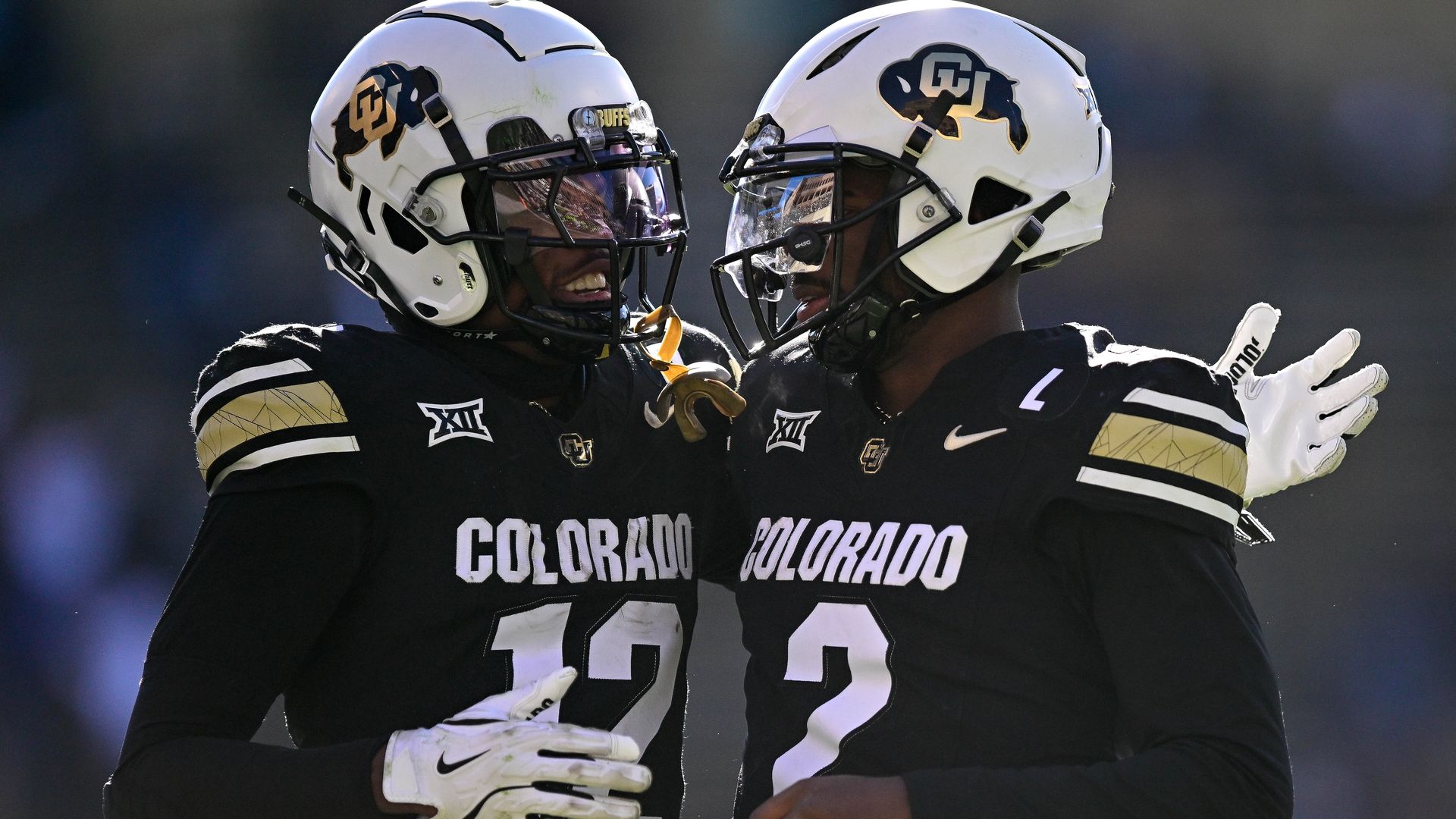 Two Colorado college football players embrace on field. 