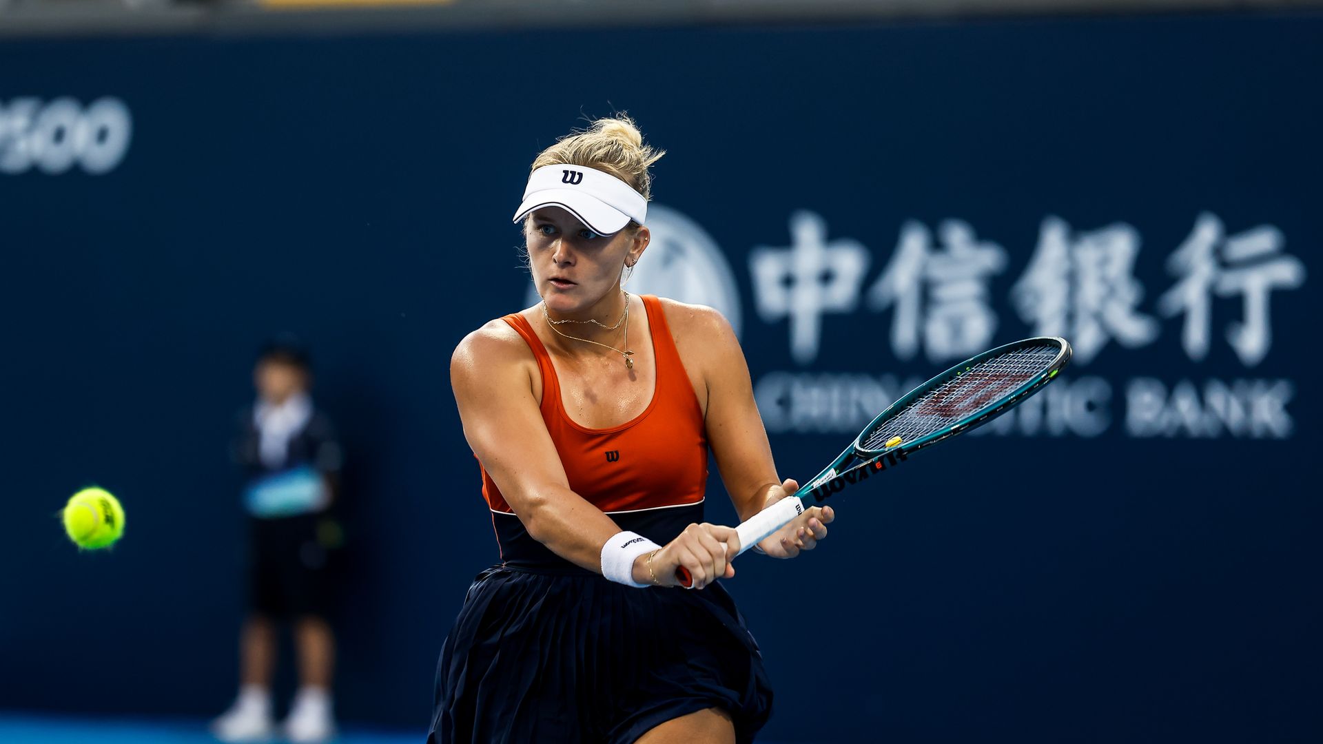 Tennis player in orange top and black skirt hits a backhand shot on a blue court, with a yellow tennis ball approaching and Chinese and English text on a dark blue background.
