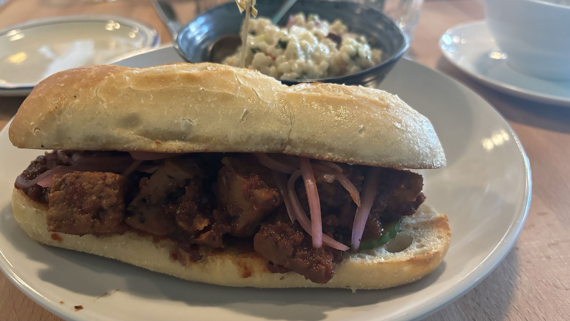 A sandwich on a plate with a salad behind it. 