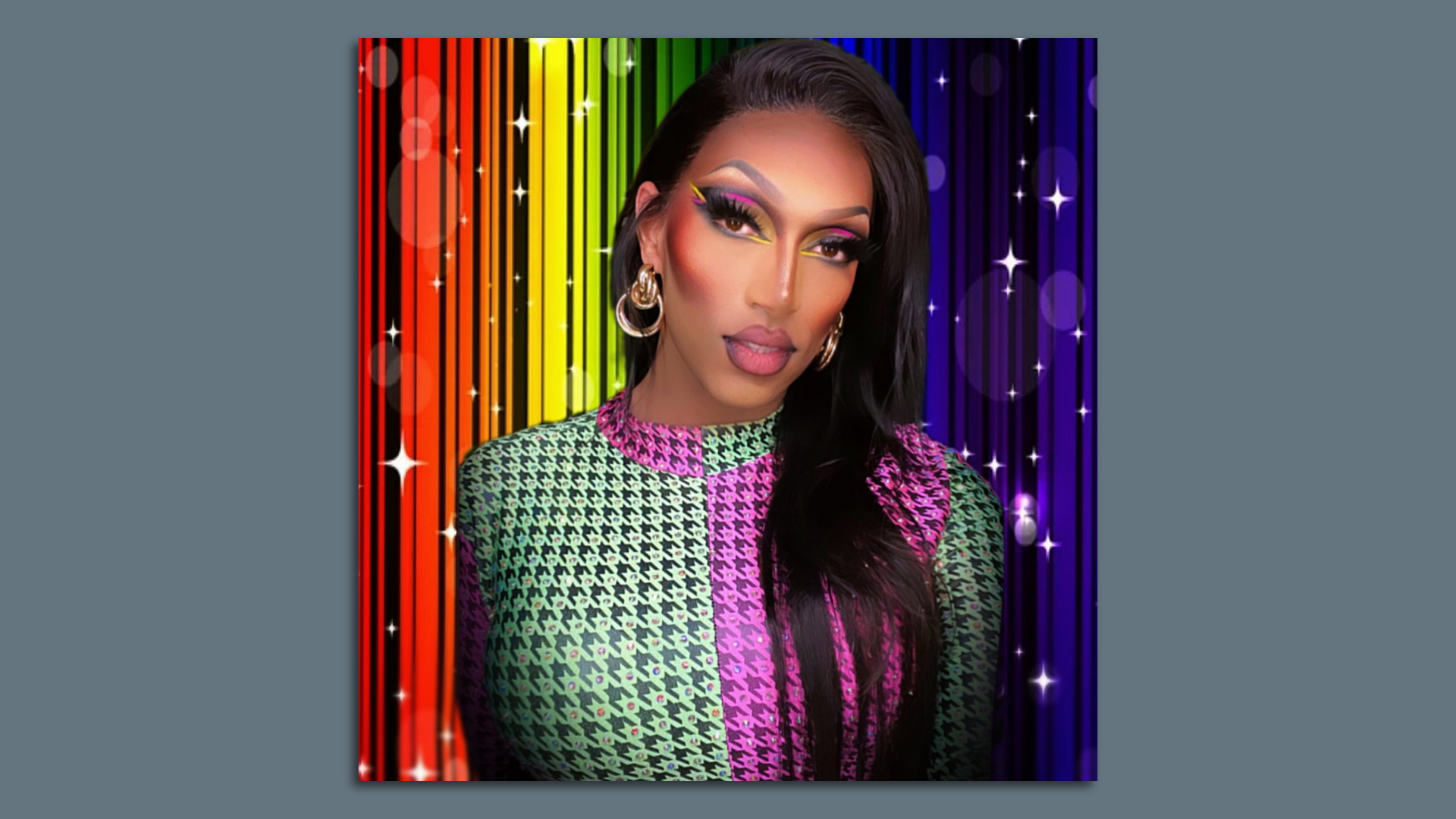 A woman with long black hair, wearing a green and magenta top, poses in front of a sparkly rainbow  background.