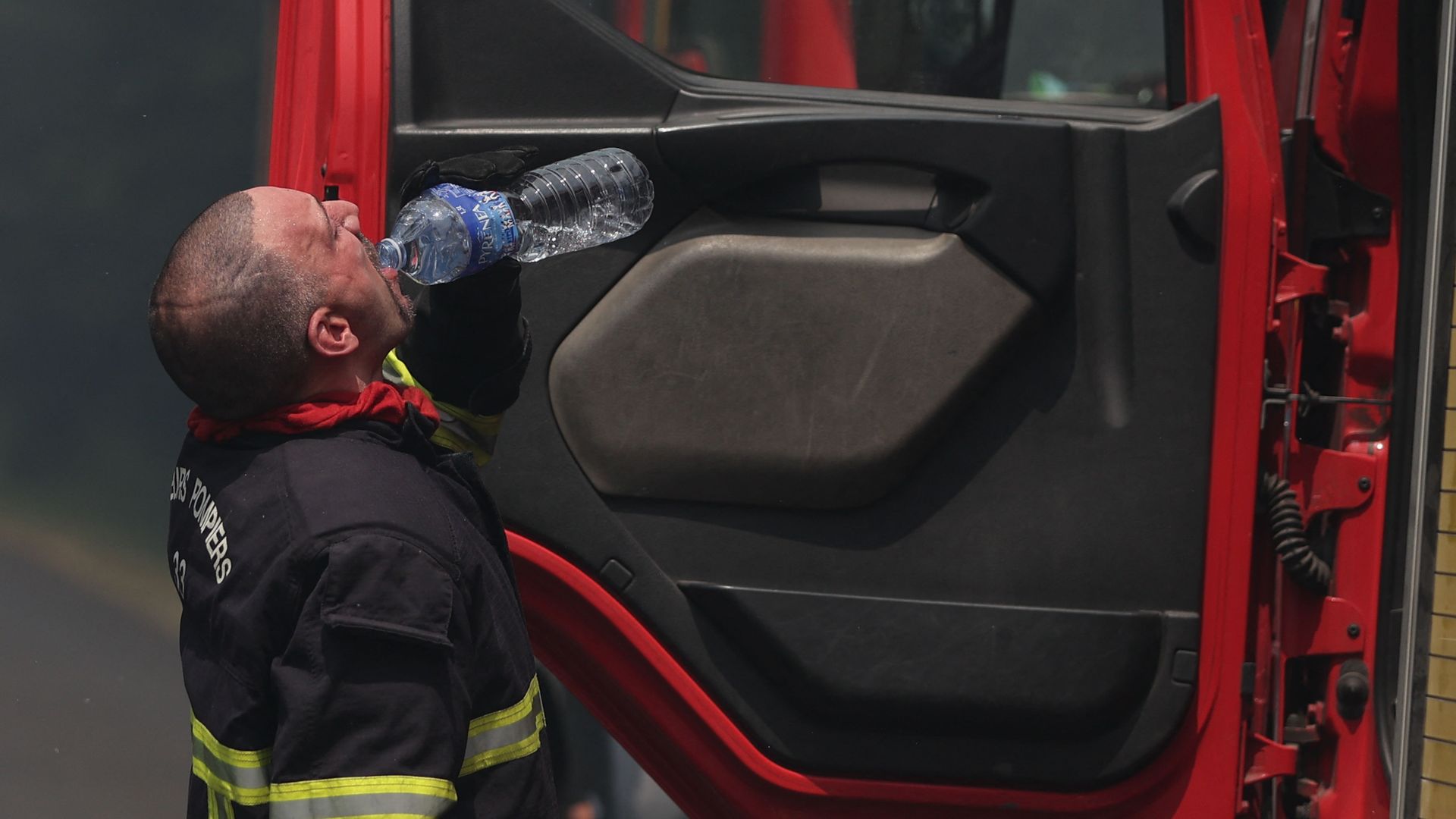 Photo of a firefighter drinking water while fighting a wildfire during a heat wave.