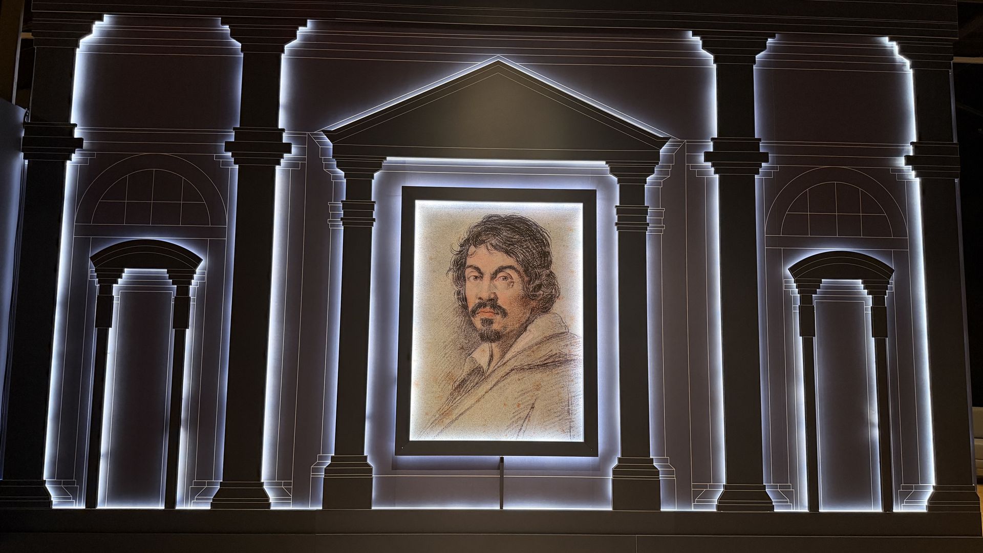 Symmetrical interior display with tall classical columns and arches, glowing neon outlines, and a central framed sketch of a bearded man with wavy hair.